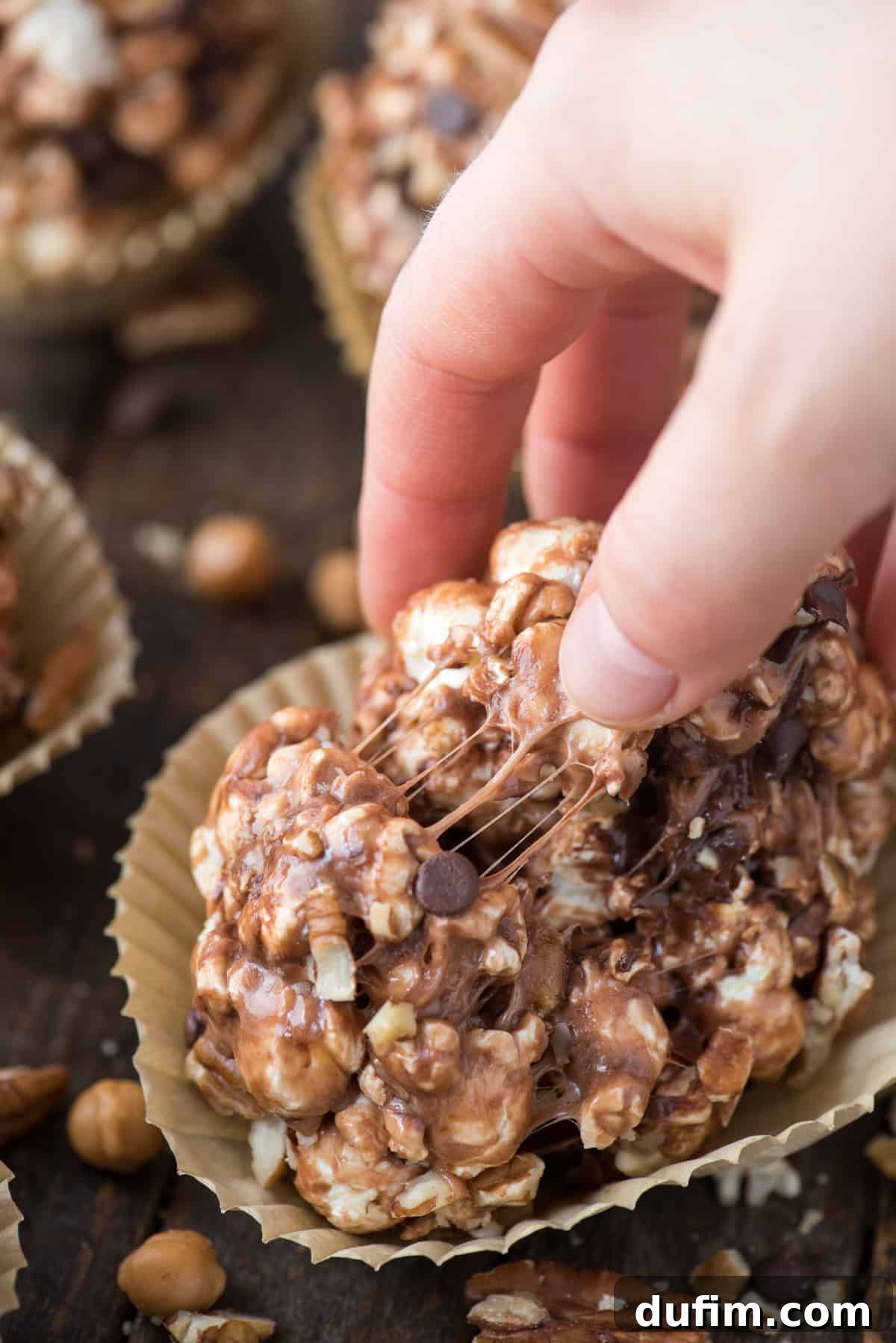 A perfectly formed turtle popcorn ball, rich with caramel, chocolate, and pecans, held gently in a hand, highlighting its delightful texture and generous toppings.