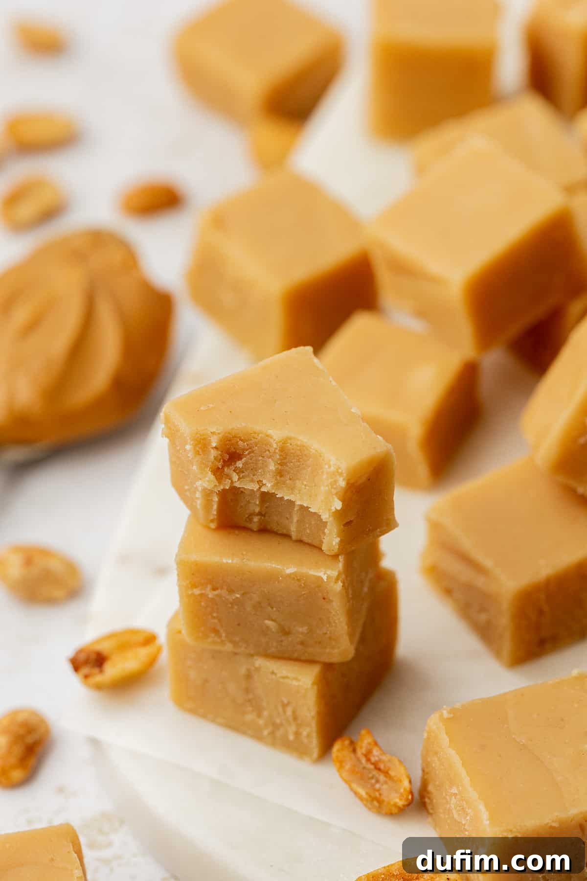Three pieces of peanut butter fudge stacked, with one piece having a bite taken out, showing its creamy interior