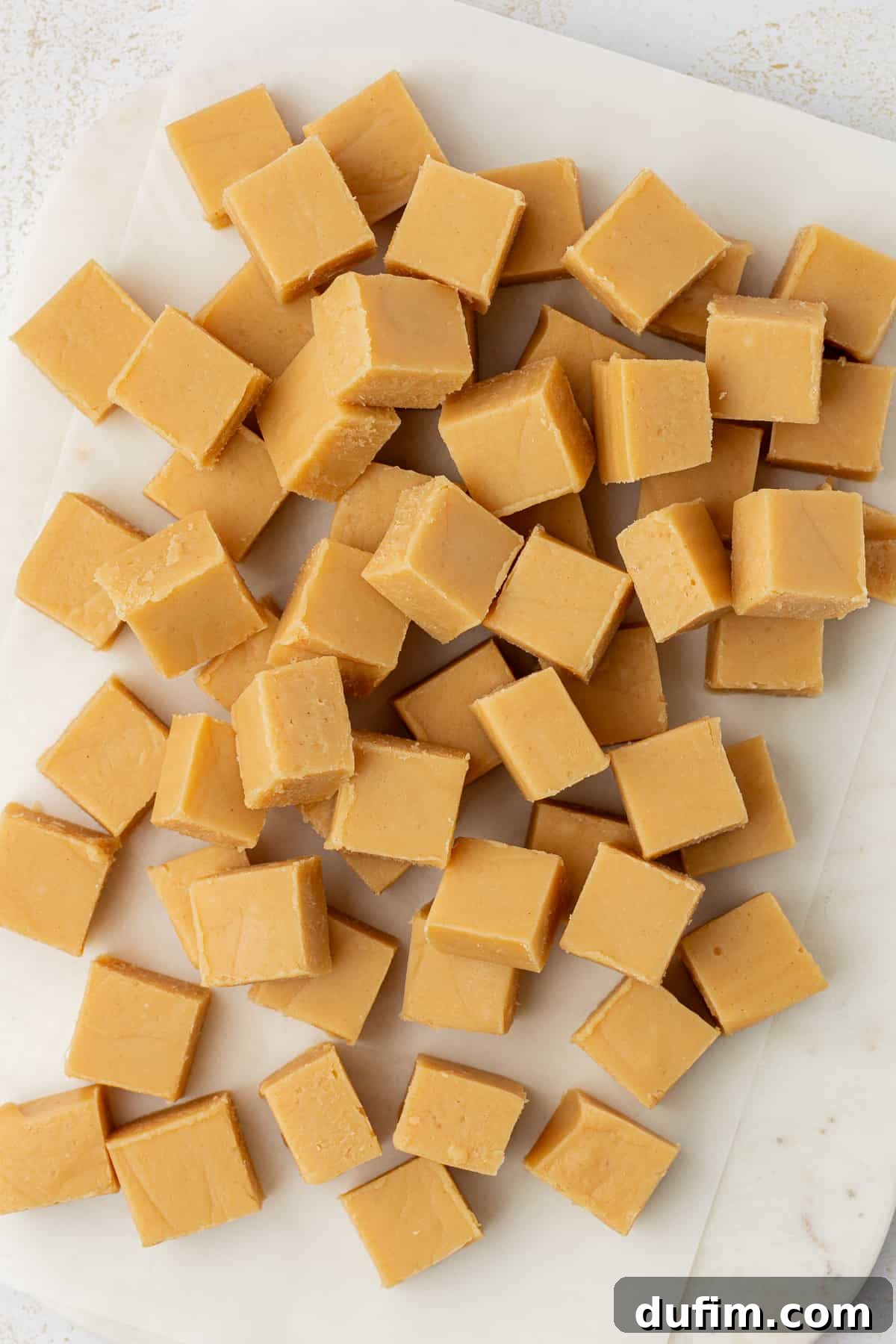 Small, perfectly cut squares of peanut butter fudge arranged neatly on white parchment paper