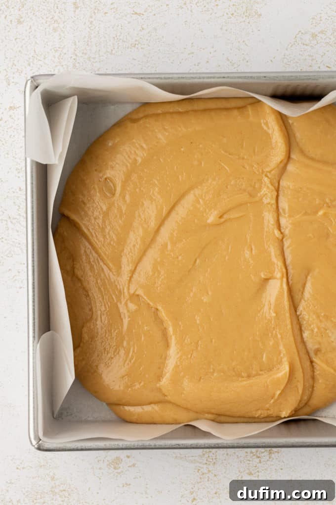 Freshly poured peanut butter fudge setting in an 8x8 inch metal pan lined with parchment paper