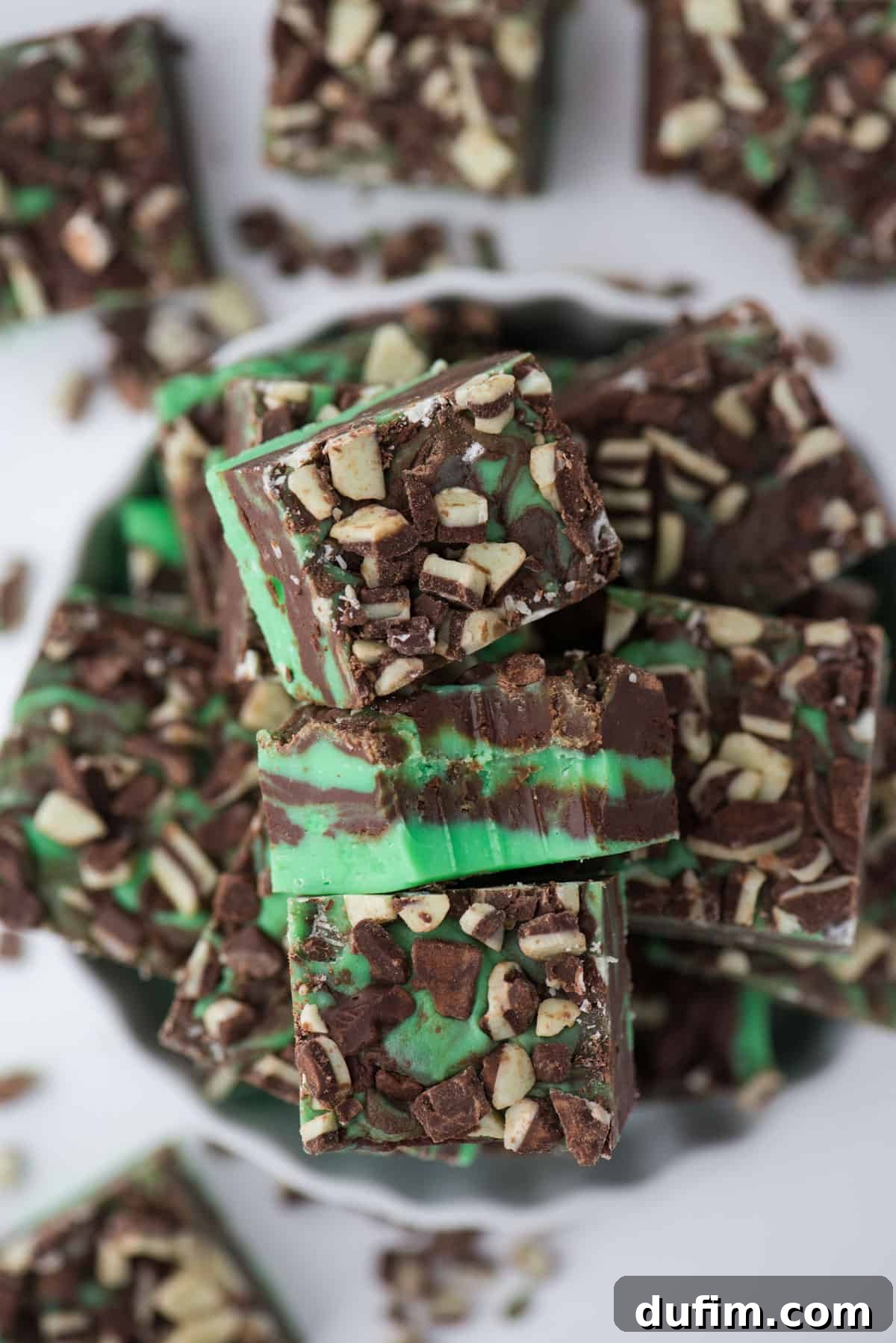 Vibrant green and brown mint chocolate fudge pieces in a pristine white bowl, showcasing the dessert's irresistible texture and holiday appeal.