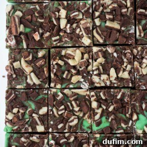 Squares of mint chocolate fudge topped with chopped chocolate pieces, arranged in a grid pattern. The rich fudge features a green mint chocolate layer beneath the decadent candy topping for a visually striking treat.