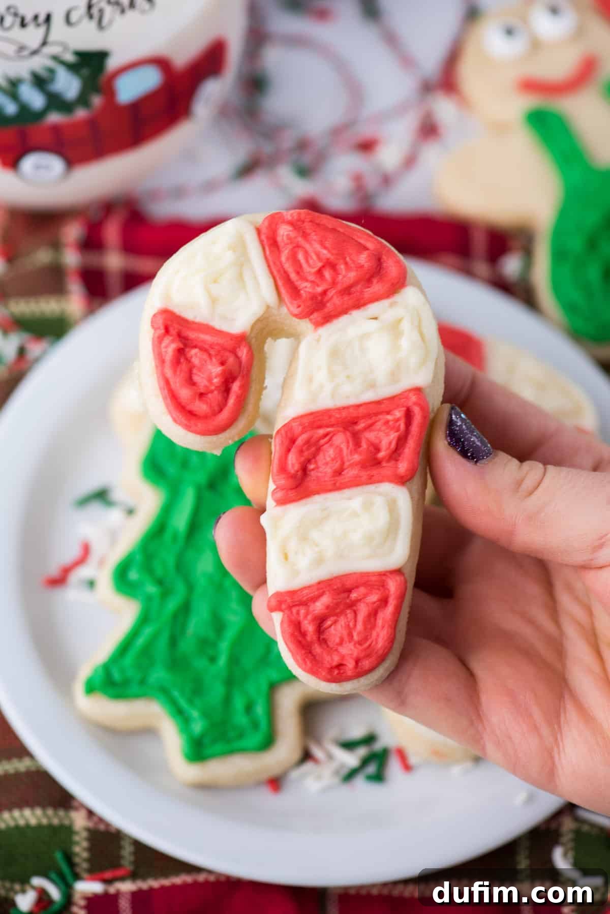 A hand gently holding a beautifully decorated candy cane sugar cookie, showcasing its perfect cut-out shape and festive icing. 