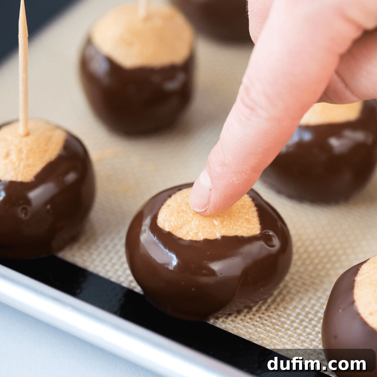 Sweet & Salty Homemade Peanut Butter Buckeye Bites 9 A freshly dipped peanut butter ball, with a finger gently covering the hole left from the toothpick, demonstrating the finishing touch.