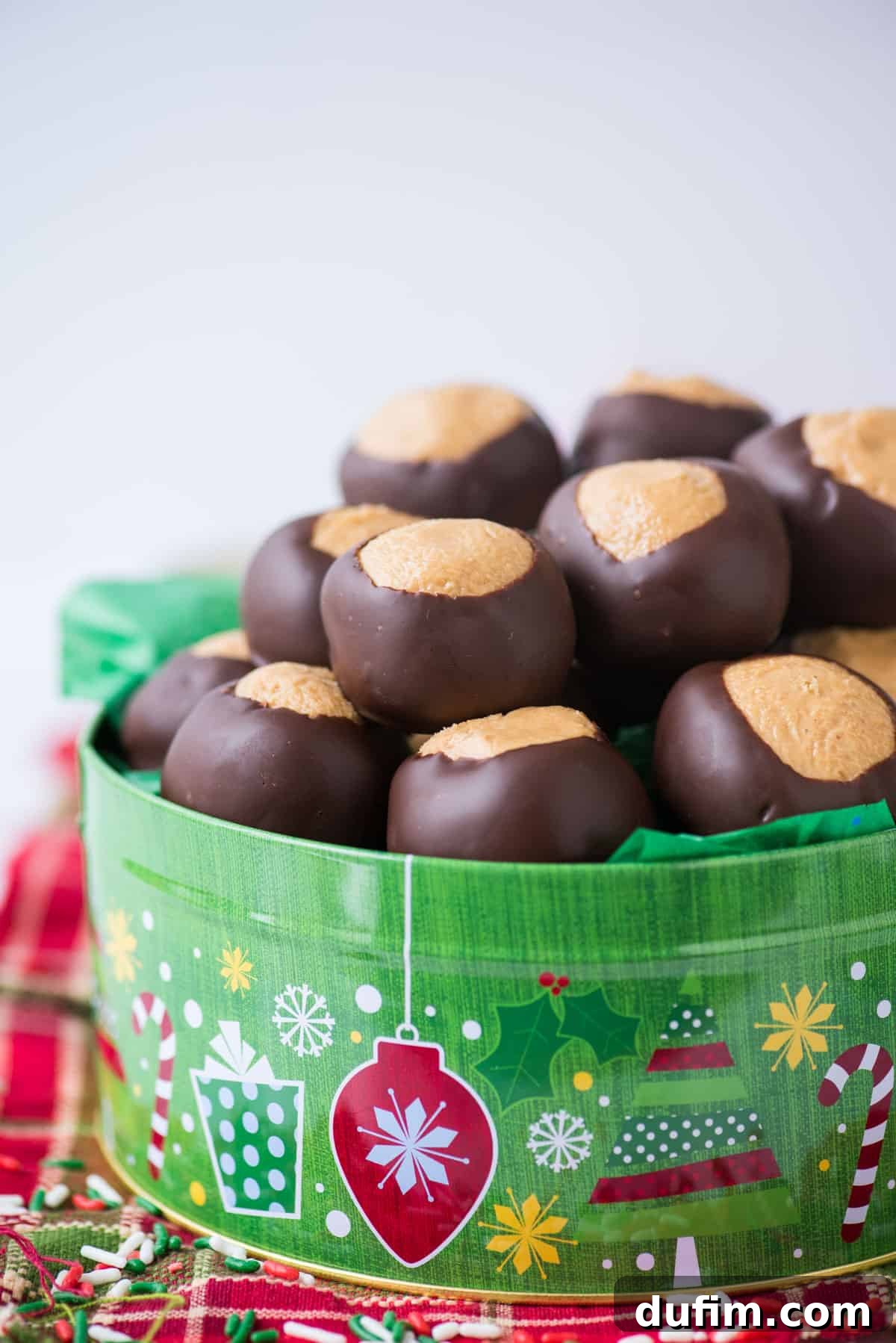 Sweet & Salty Homemade Peanut Butter Buckeye Bites 10 Finished peanut butter balls nestled charmingly in a green Christmas cookie tin, resting on a red striped towel.