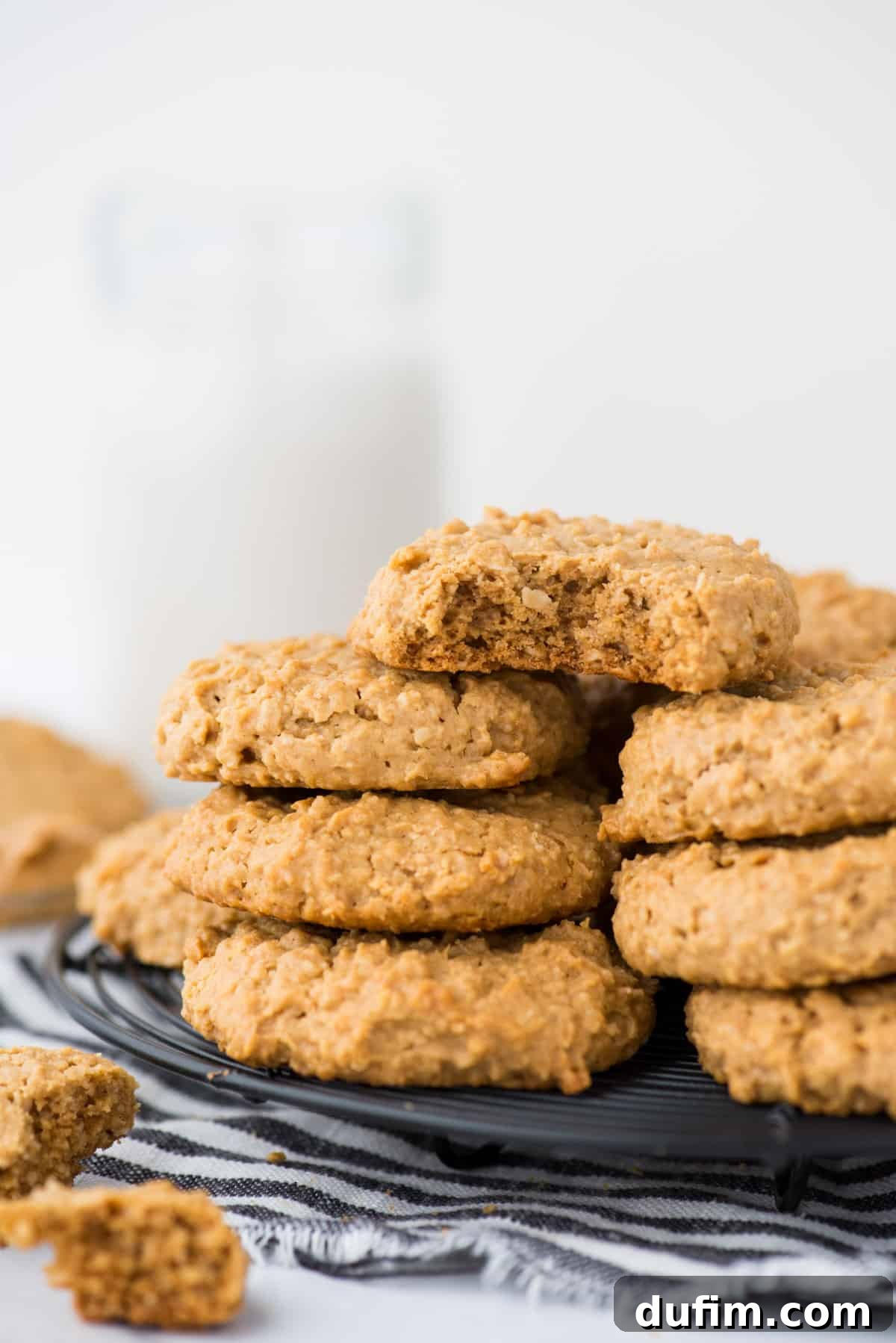 Guilt-Free Peanut Butter Oatmeal Treats 2 A stack of golden brown healthy peanut butter cookies on a black wire cooling rack, set against a pristine white background. The cookies exhibit a perfect criss-cross fork pattern.