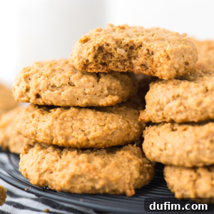 A stack of thick, golden brown healthy peanut butter cookies sits on a wire cooling rack, with one cookie on top showing a bite taken out. The cookies look soft and chewy.