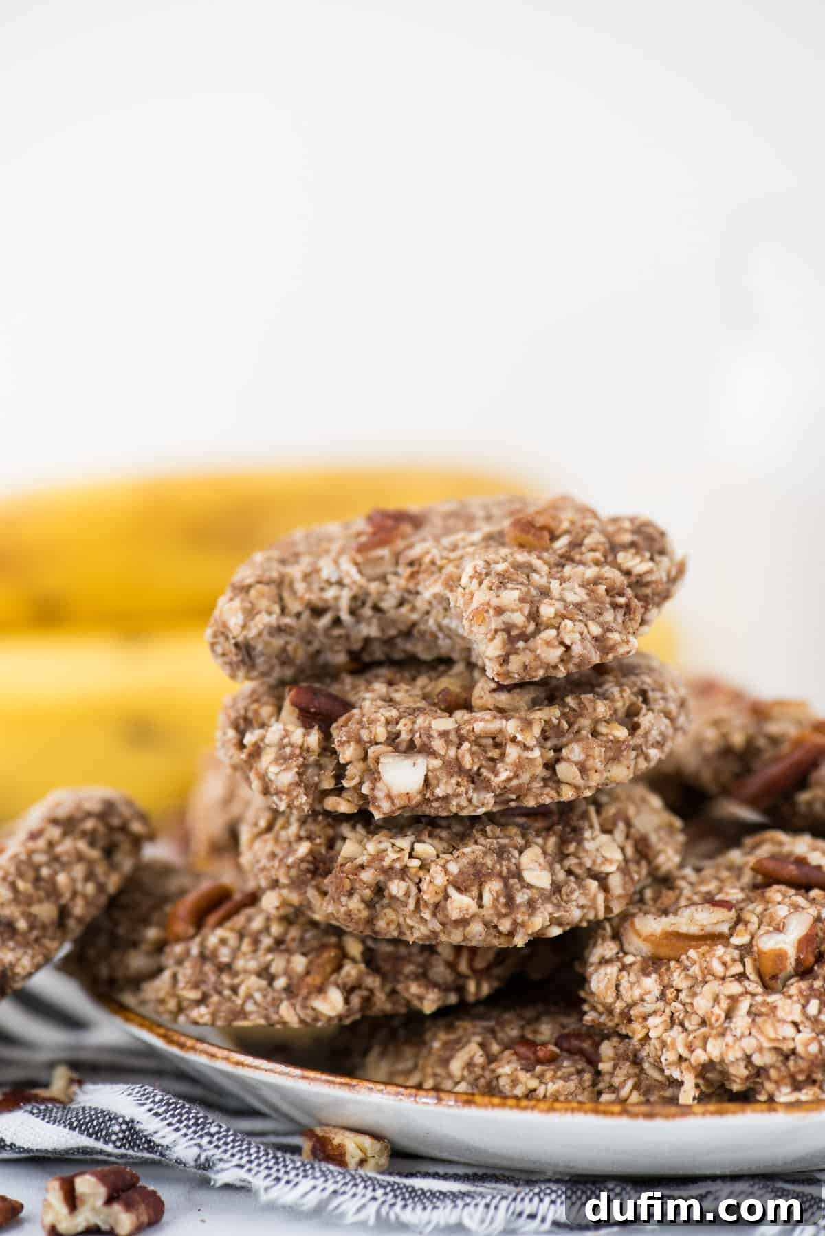 A stack of healthy banana breakfast cookies on a white plate, with a striped towel underneath