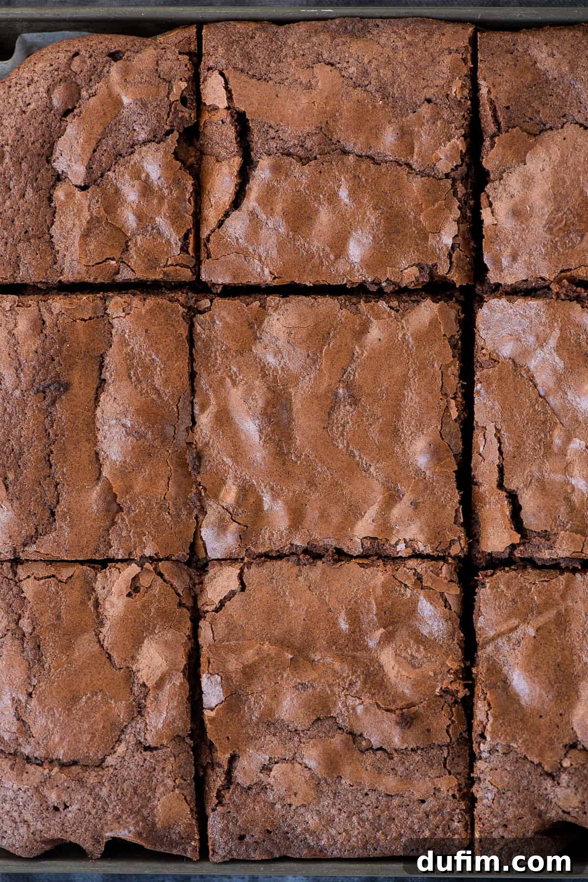 A baking pan filled with freshly baked brownies, neatly cut into squares, showing their perfectly fudgy centers and crackled tops.