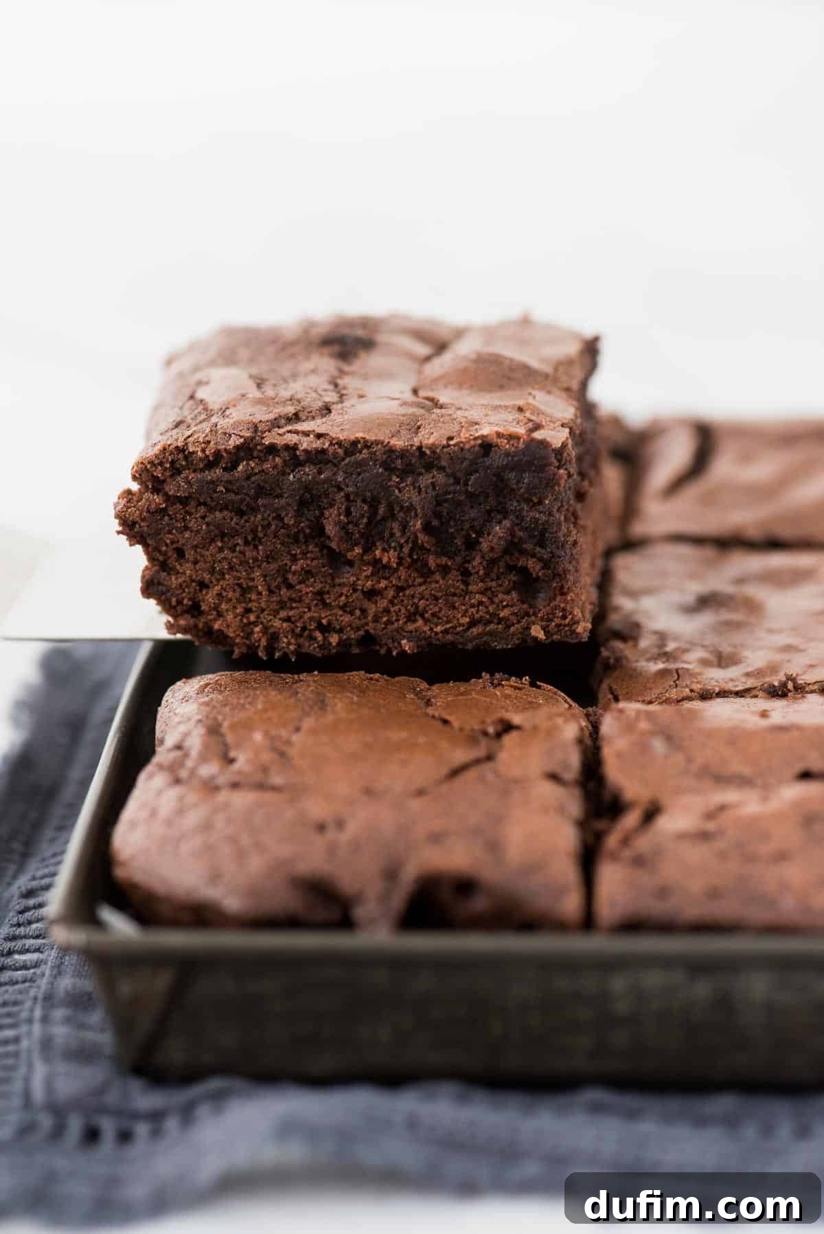 A metal spatula gently lifting a warm, fudgy brownie square from the baking pan, showing its perfect shape and moist interior.