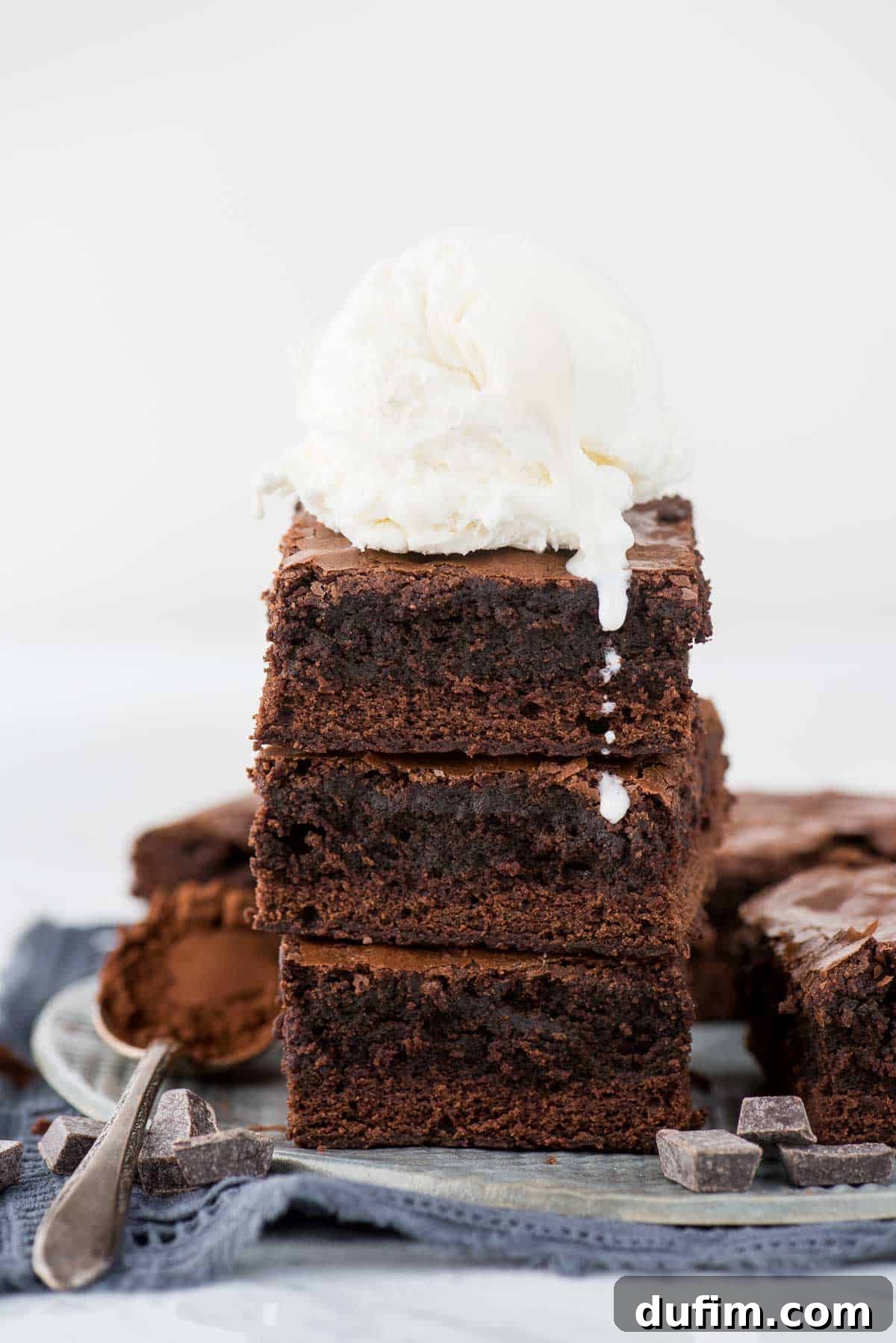 A stack of three decadent brownies topped with a scoop of creamy vanilla ice cream, creating a classic warm and cold dessert.