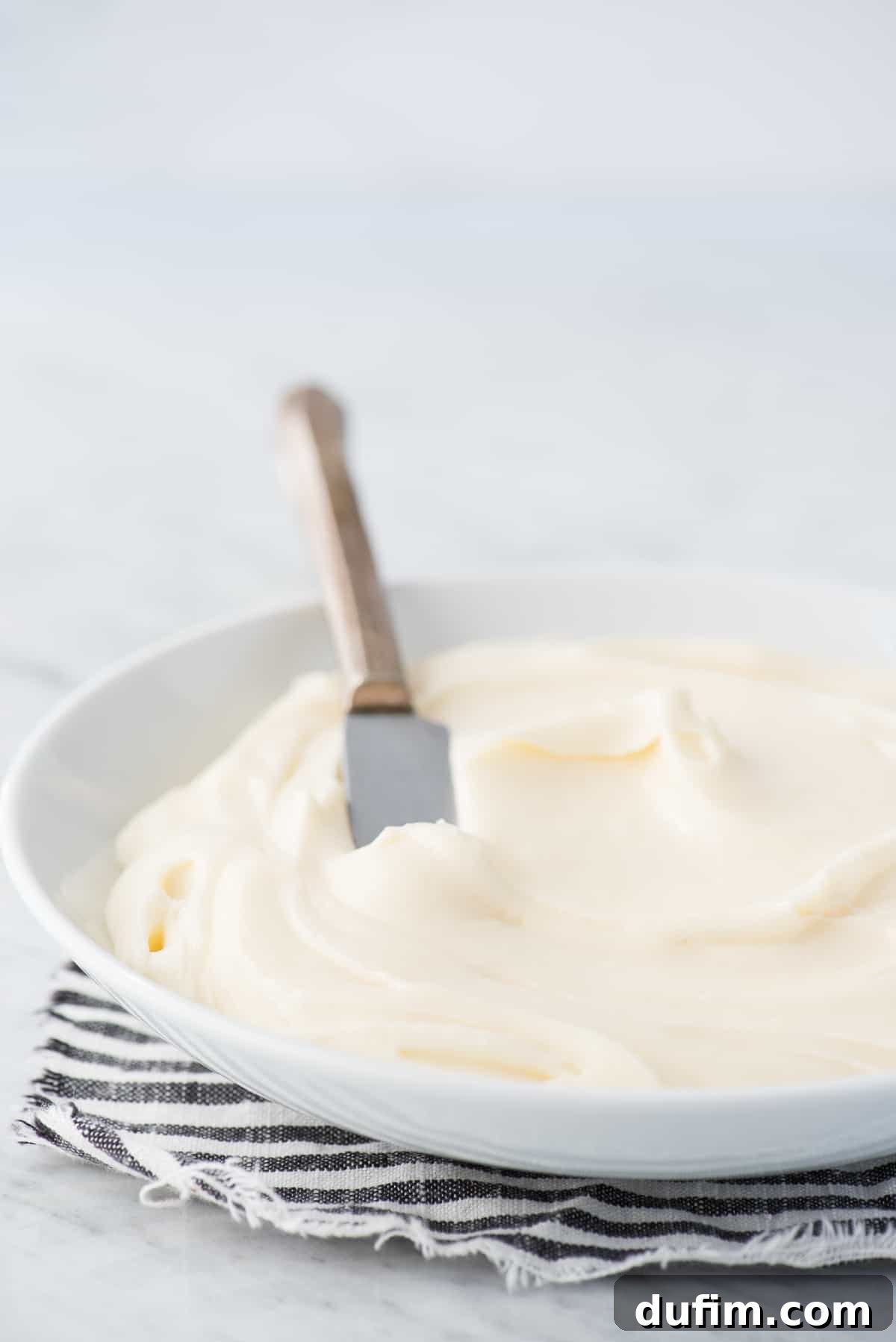 Homemade Cream Cheese Frosting Perfection 7 Cream cheese frosting in a white bowl with a metal knife.