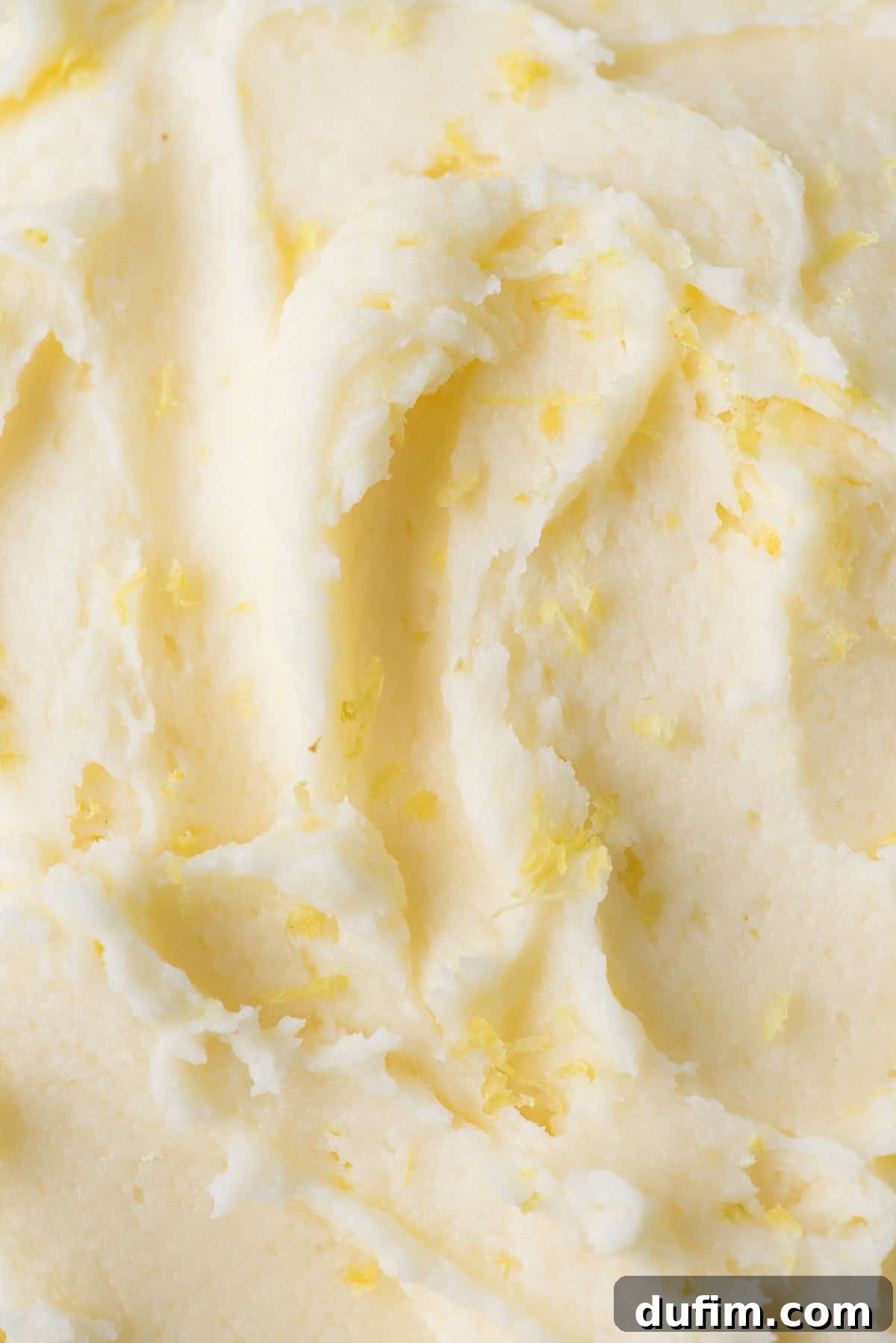 Close-up of fluffy lemon frosting garnished with fresh lemon zest, highlighting its smooth texture and vibrant color.