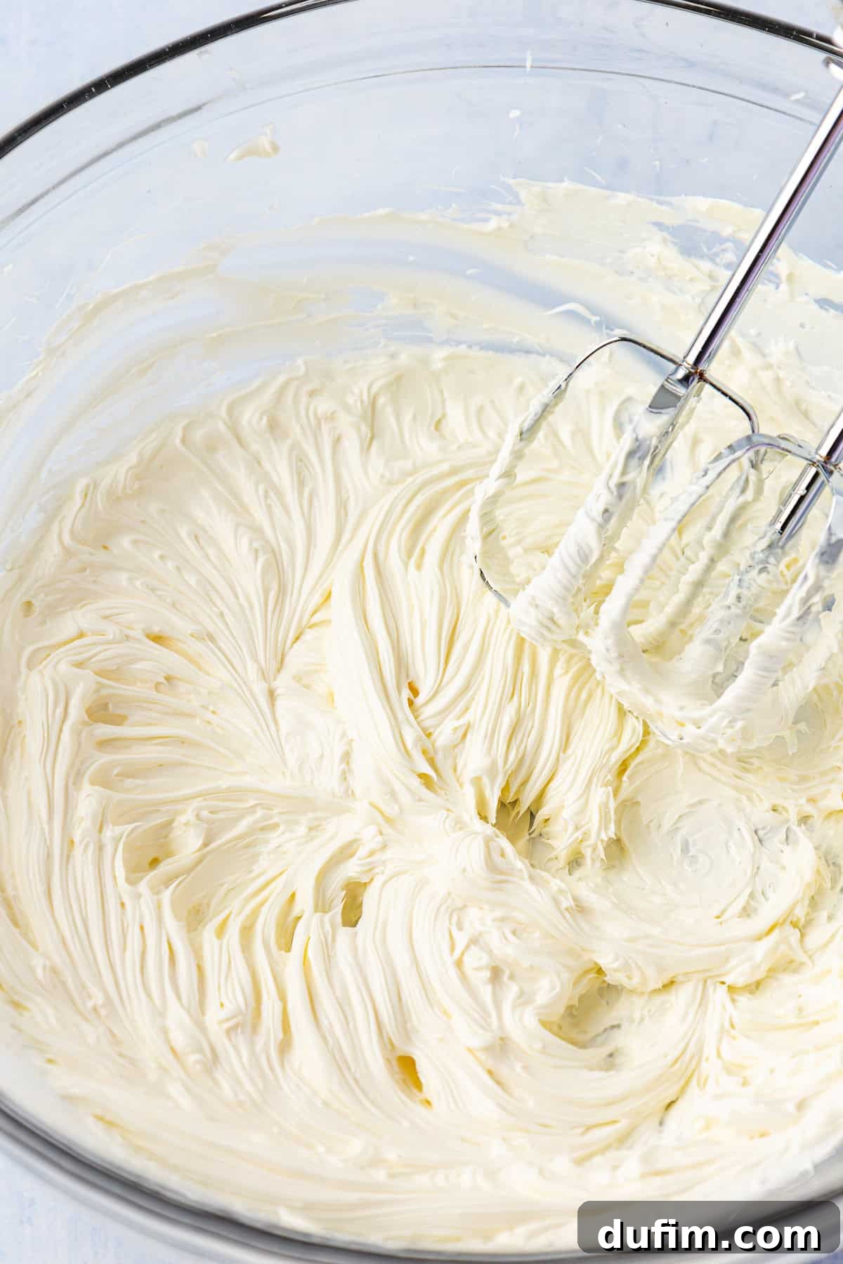 Butter creaming in a clear glass bowl with an electric mixer, becoming light and fluffy.