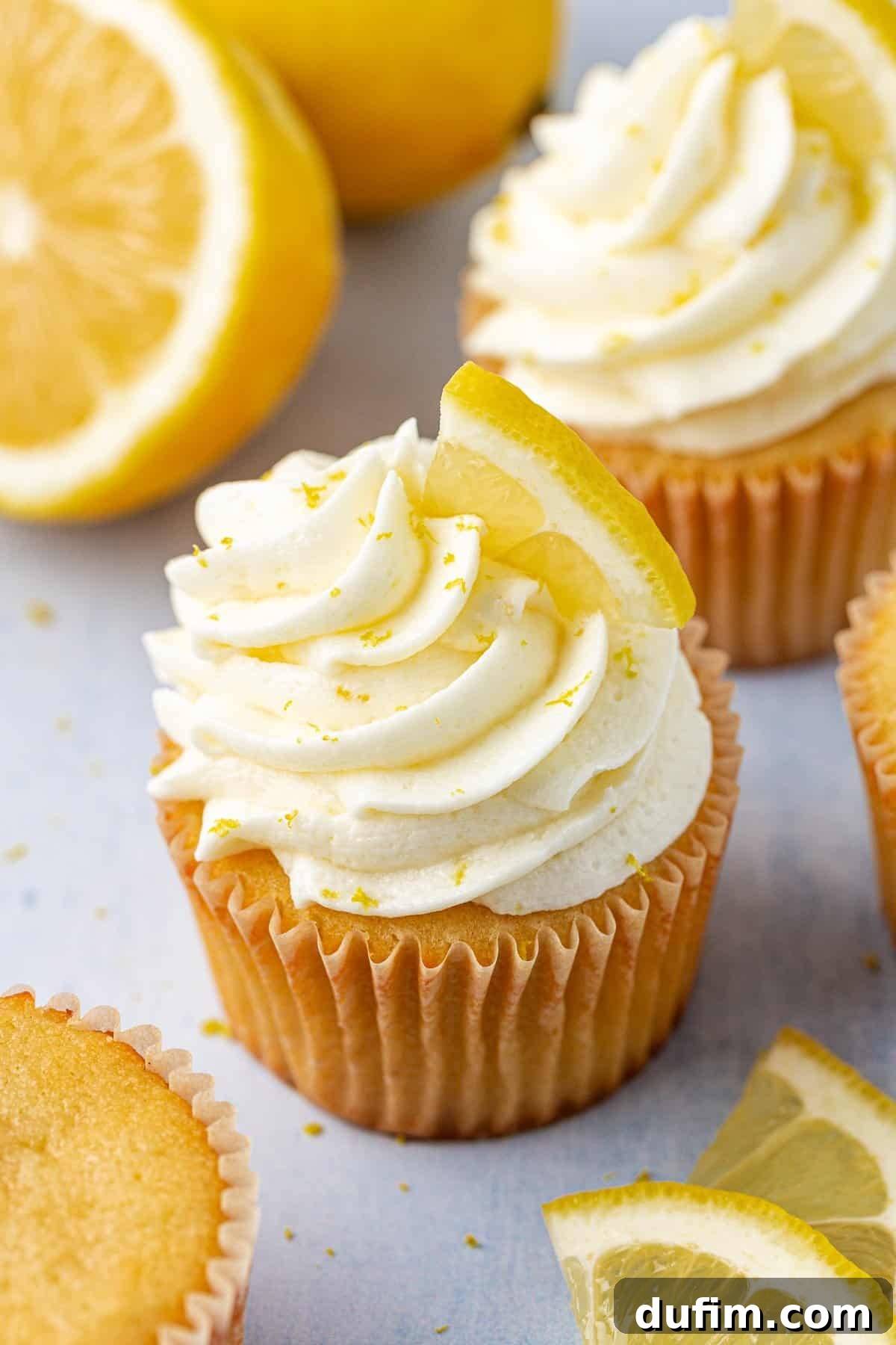 Delicious cupcakes topped with vibrant lemon frosting, garnished with delicate lemon slices and finely grated lemon zest.