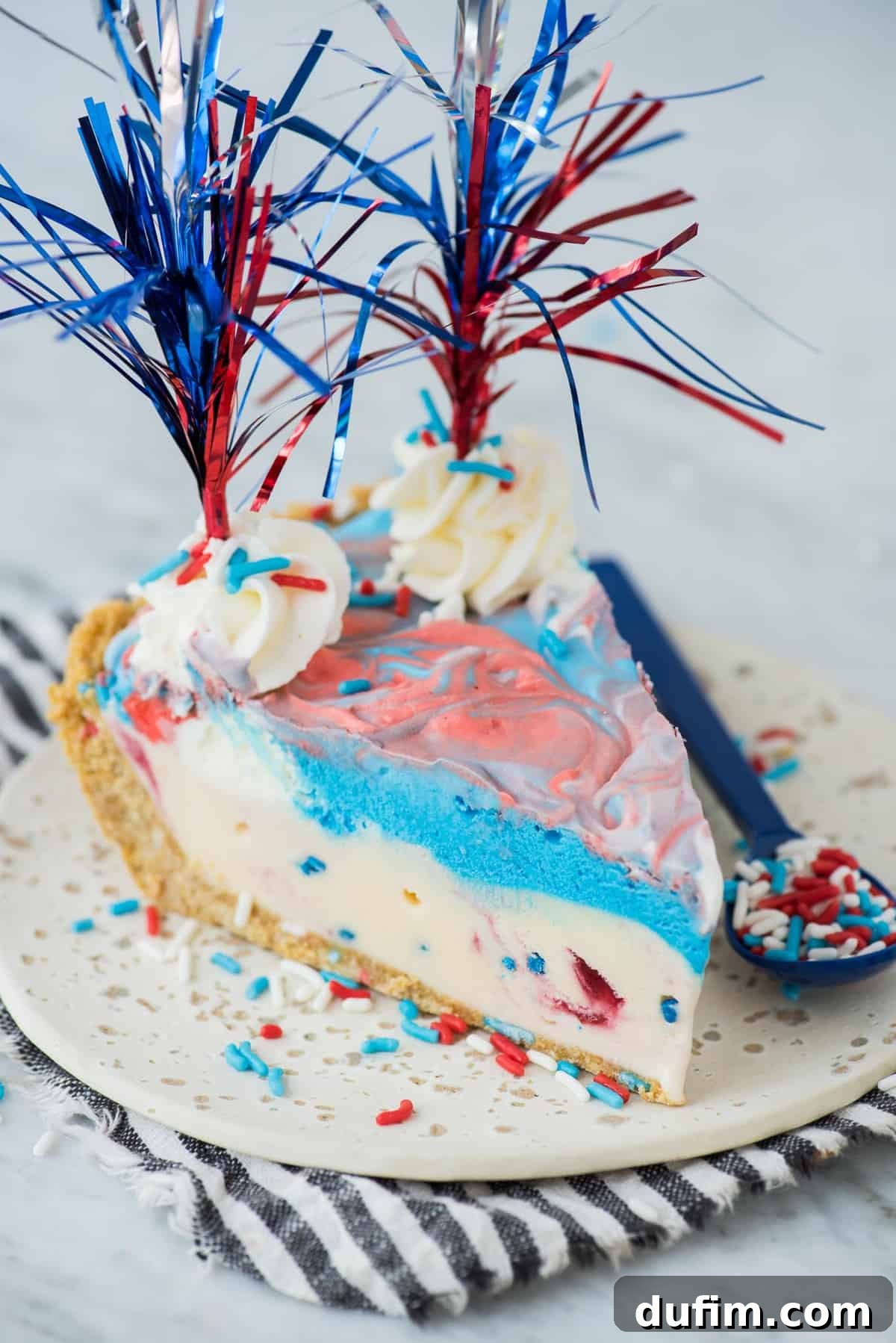 Slice of 4th of July red, white and blue ice cream pie on a white plate with a blue stripe napkin, ready to be enjoyed.