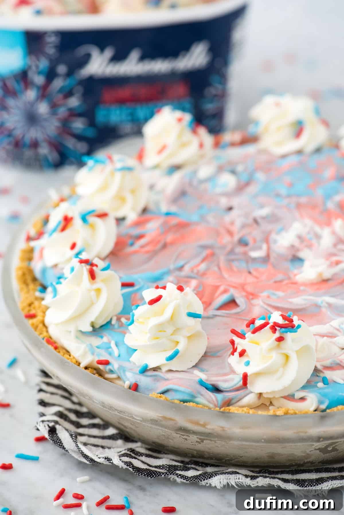 Full 4th of July red, white and blue ice cream pie on a blue stripe napkin, garnished with sprinkles.