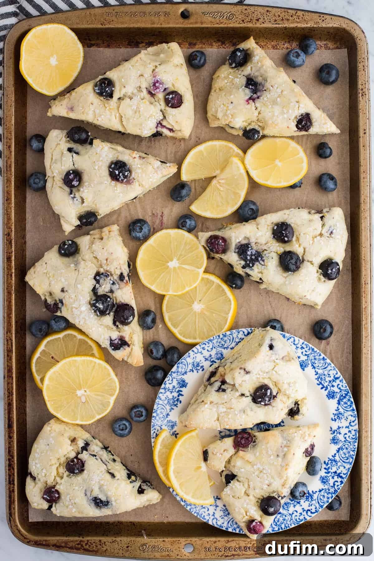A beautifully composed shot of lemon blueberry scones on brown parchment paper, artfully arranged with vibrant lemon slices and fresh blueberries, ready to be enjoyed.