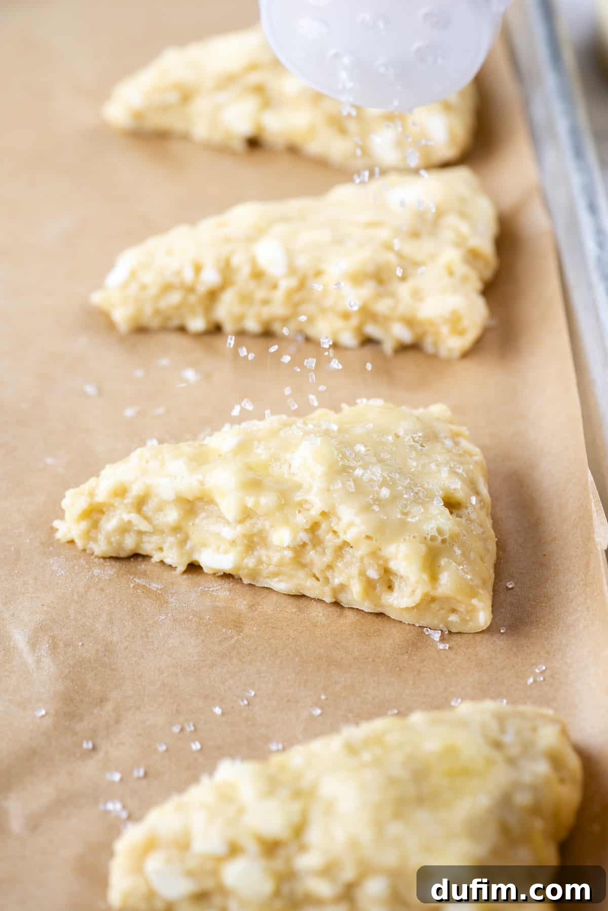 Gourmet Chocolate Chip Buttermilk Scones 11 Close-up of sanding sugar being sprinkled over unbaked chocolate chip scones on a baking sheet before they go into the oven.