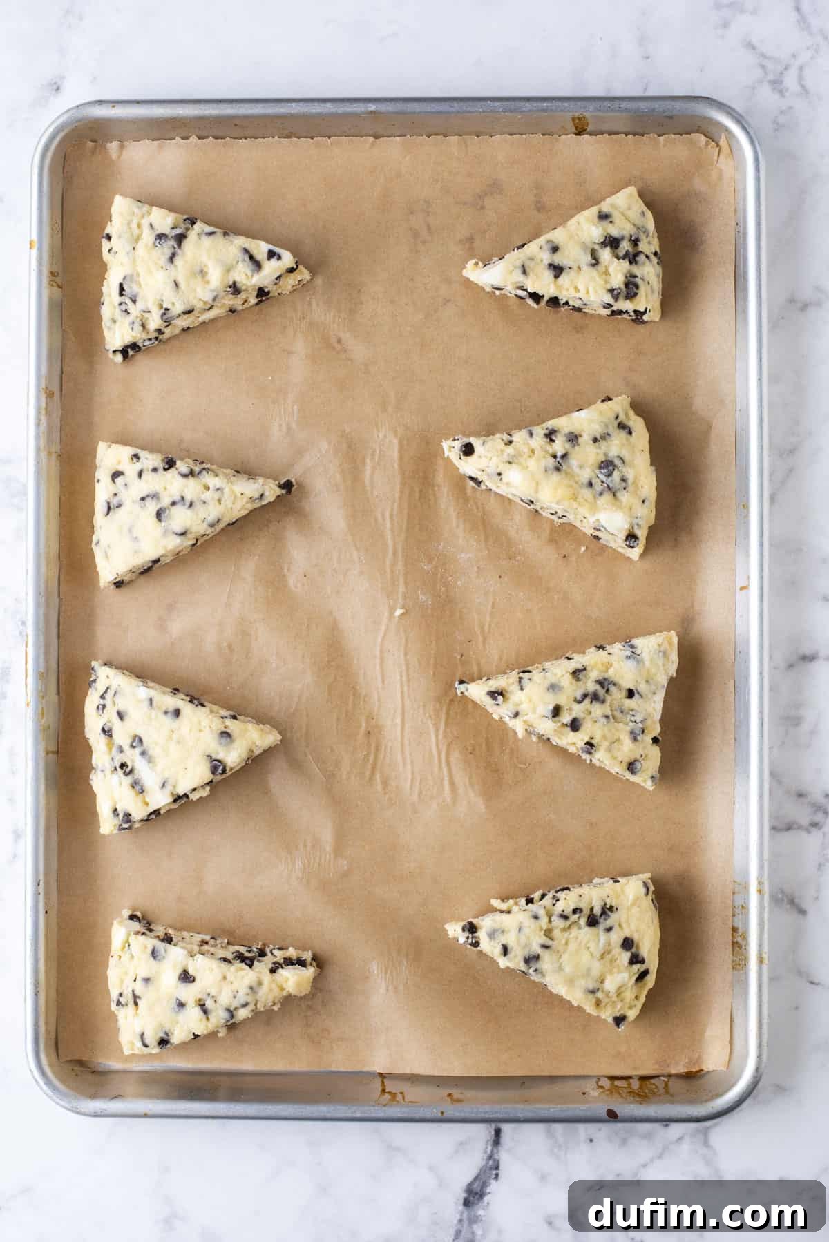 Gourmet Chocolate Chip Buttermilk Scones 12 Eight perfectly baked, golden-brown chocolate chip scones arranged on a parchment-lined baking sheet, fresh out of the oven.
