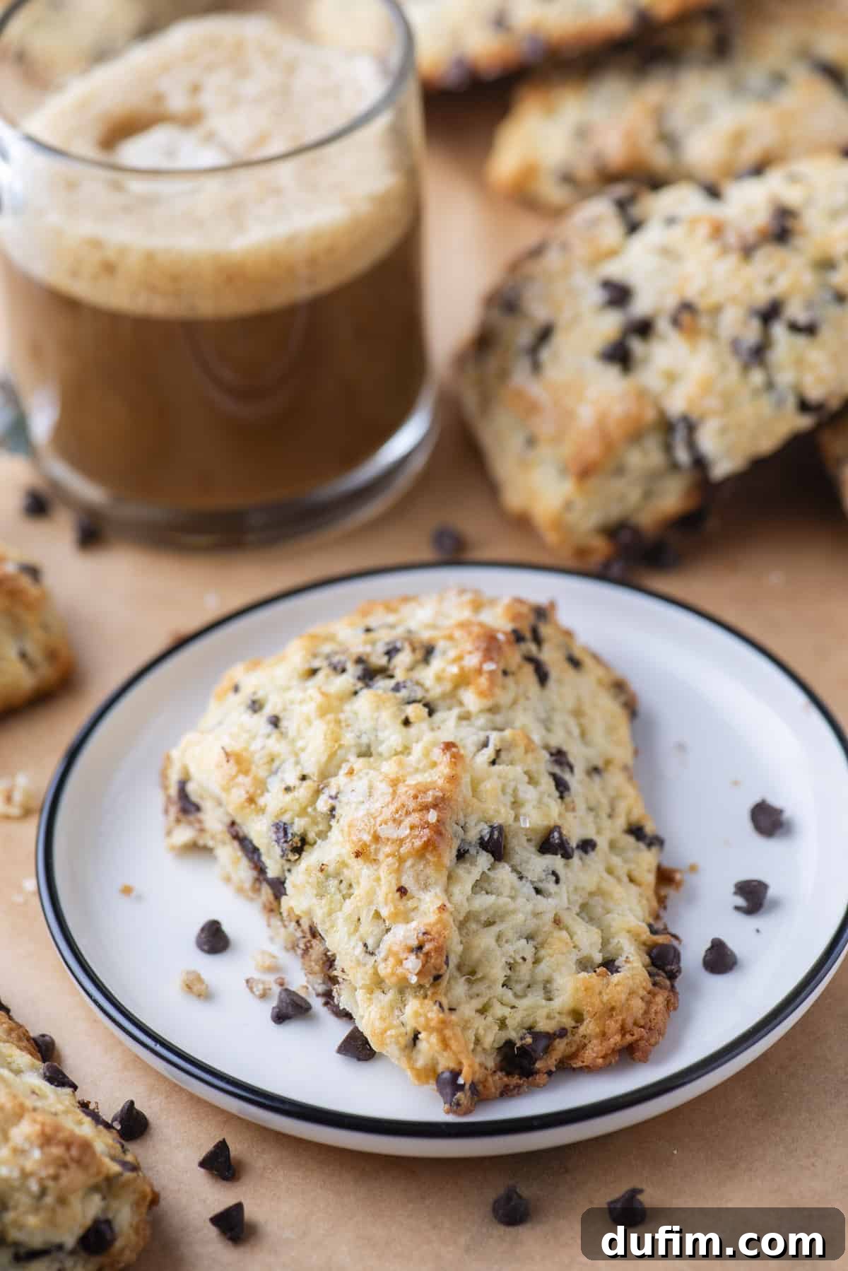 Gourmet Chocolate Chip Buttermilk Scones 4 Three chocolate chip scones on a white plate with a warm coffee mug, showcasing a cozy breakfast scene.
