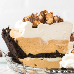 A slice of creamy no bake peanut butter pie with a chocolate cookie crust, topped with whipped cream and chopped peanut butter cups, being lifted from a glass pie dish.