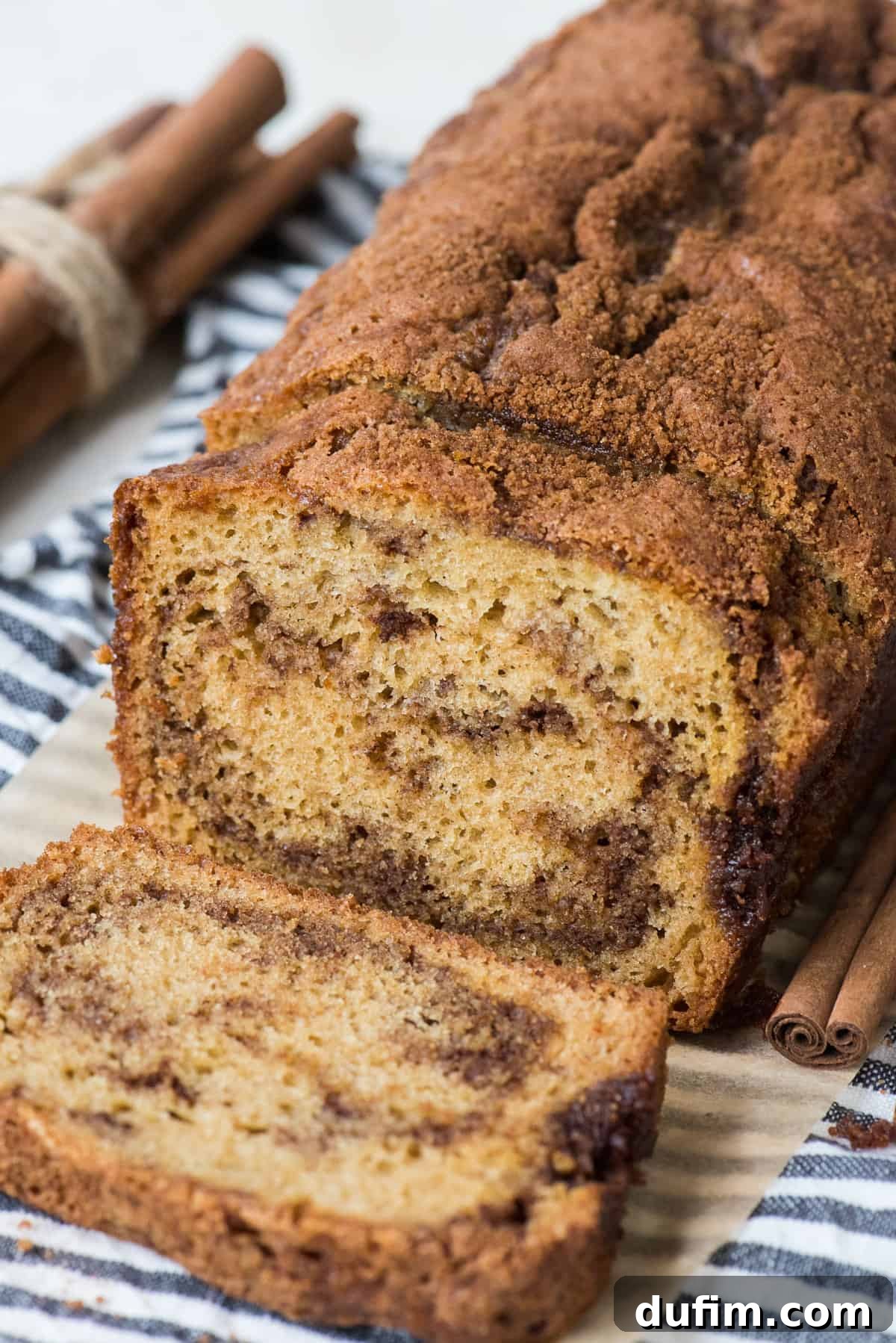 A slice of cinnamon swirl quick bread cut from a loaf, showcasing a perfect cinnamon sugar swirl, resting on a striped blue linen.