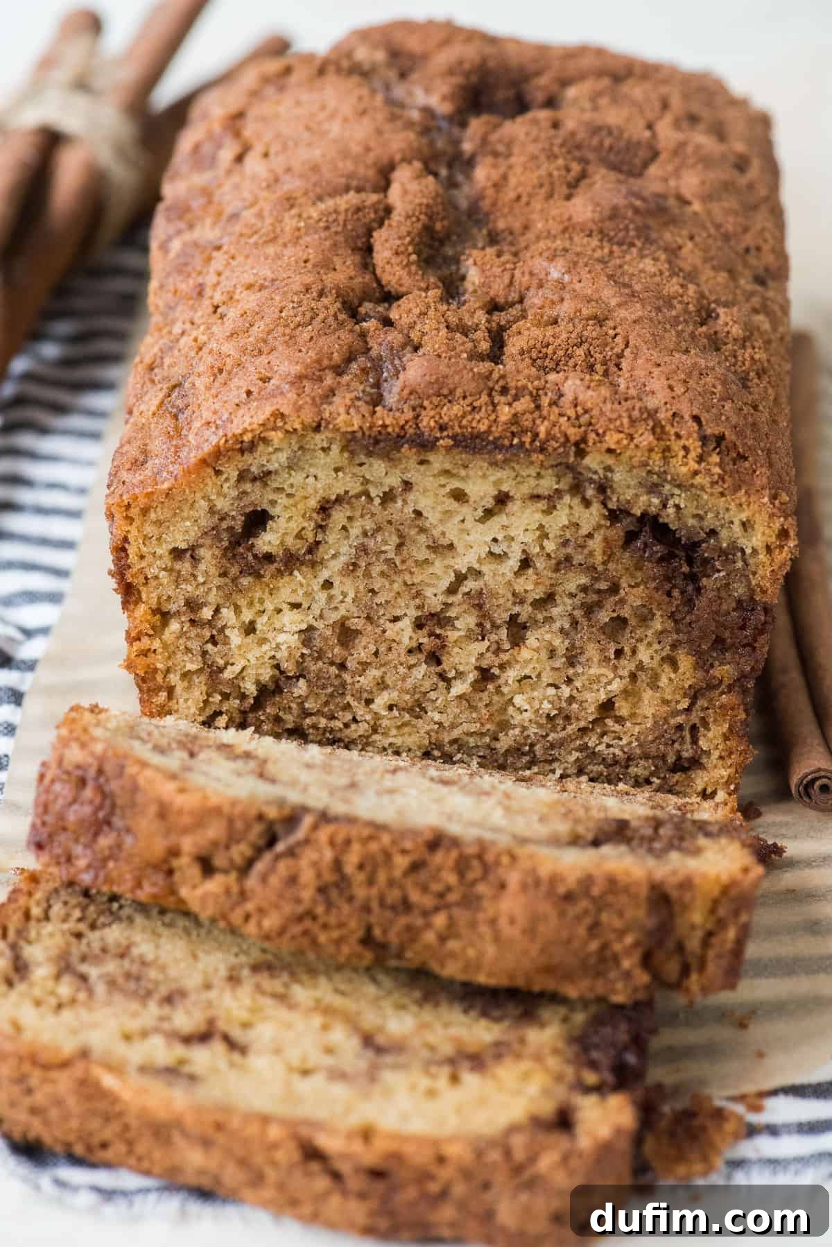 Two pieces of golden-brown cinnamon swirl bread, showing the rich cinnamon filling, served on a white plate on a blue striped linen.