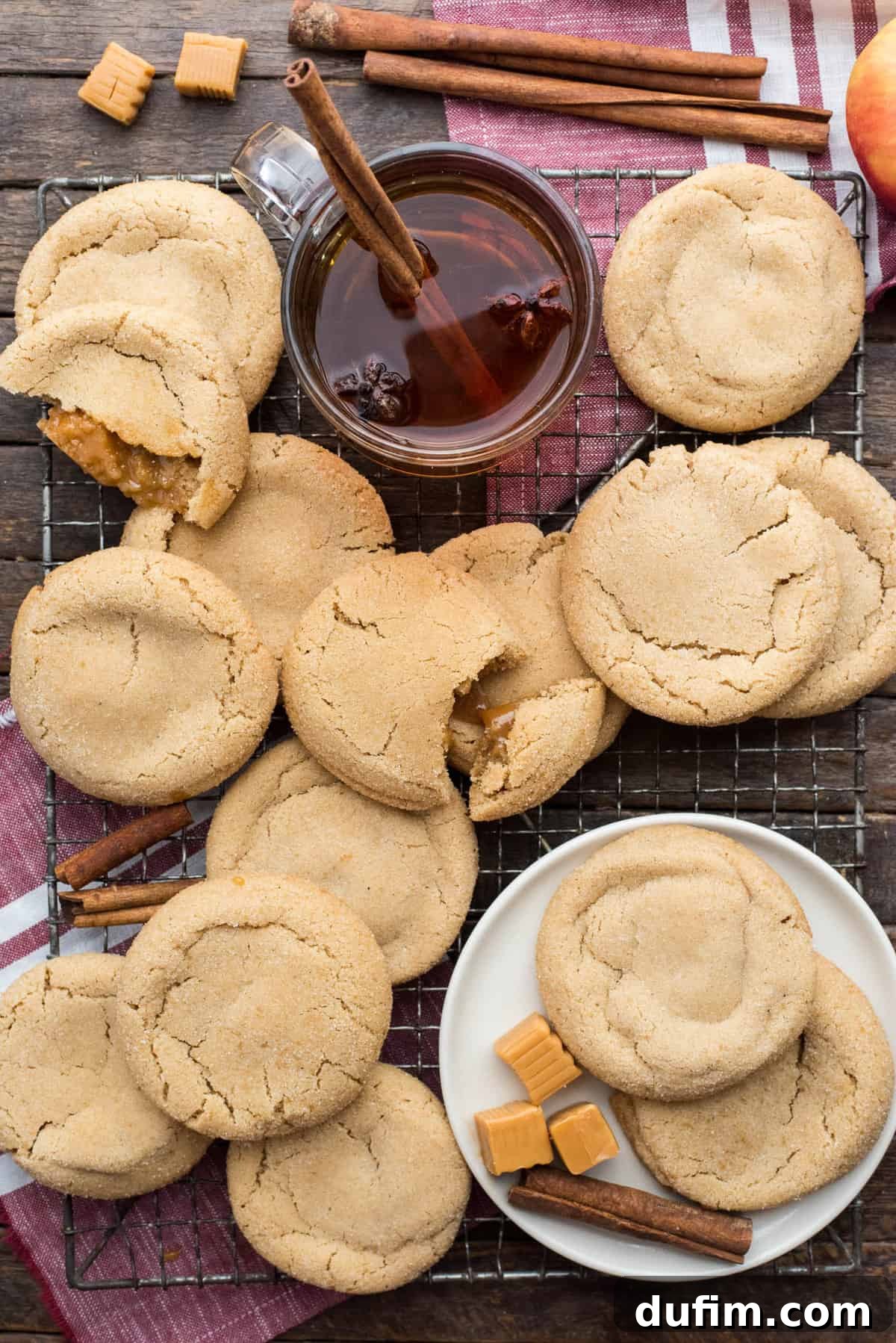 Freshly baked caramel apple cookies cooling randomly arranged on a metal baking rack against a rustic wood background.