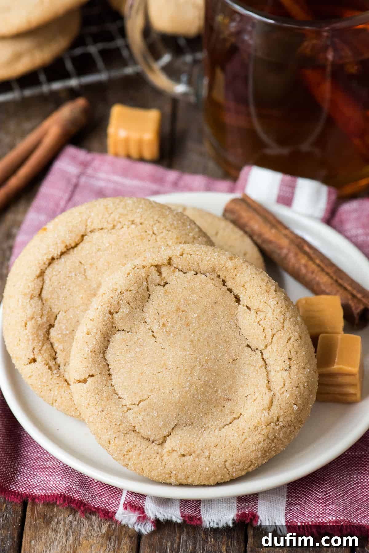 Delicious caramel apple cookies arranged on a white plate with decorative cinnamon sticks and a single caramel square in the background.