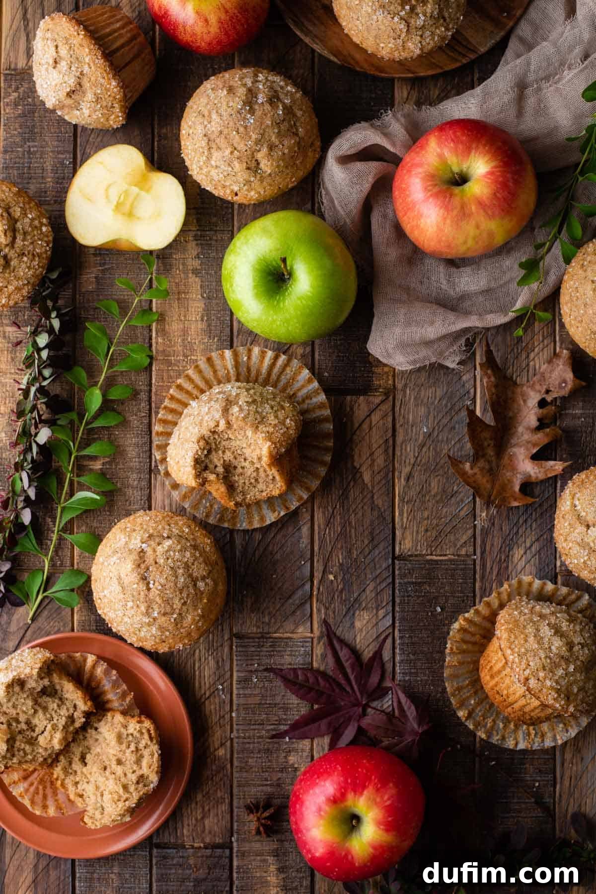 Applesauce muffins arranged on a rustic wooden background with fresh apples and vibrant fall foliage, evoking a warm autumnal scene.