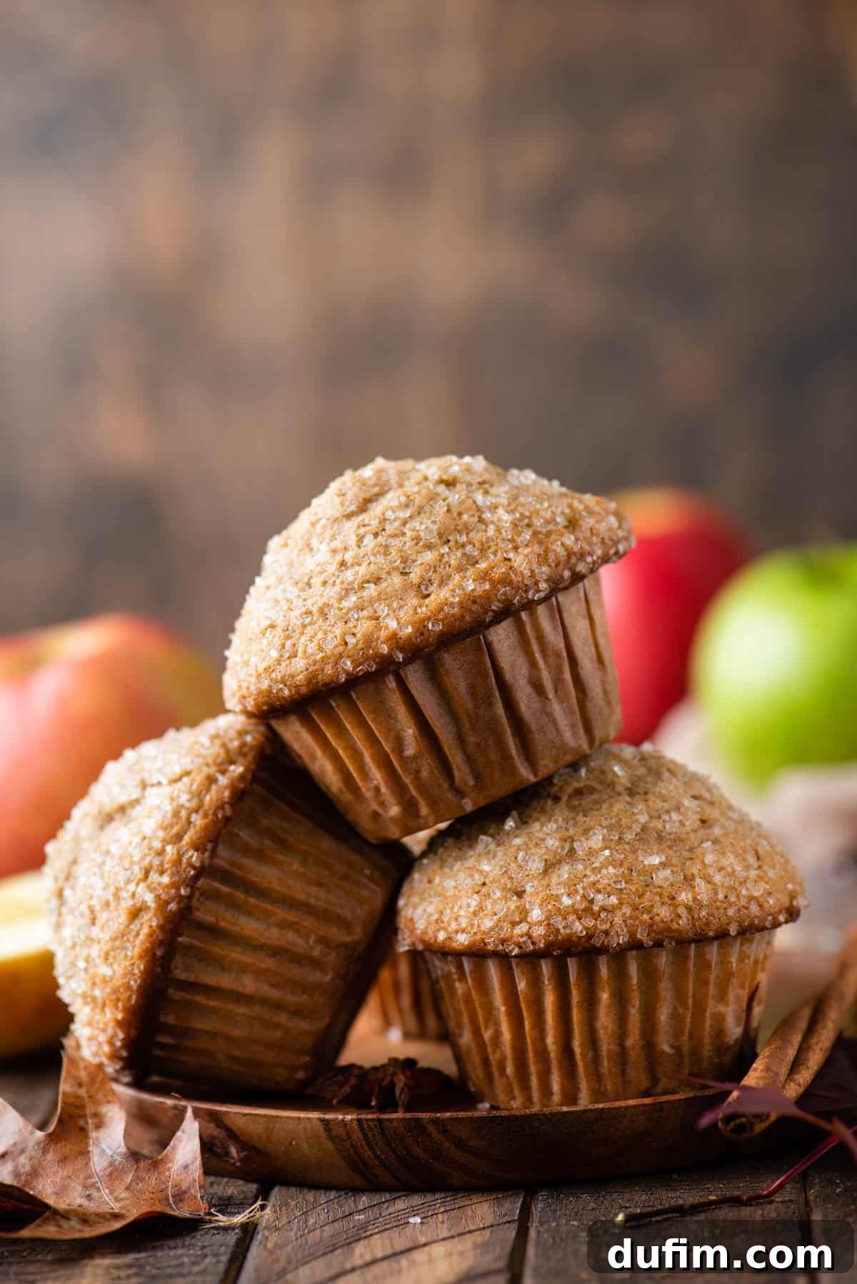 Three golden-brown applesauce muffins stacked neatly on a rustic wooden plate.
