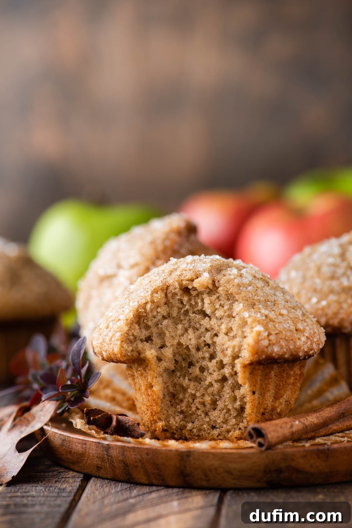 A single applesauce muffin on a wooden plate with a bite taken out, revealing its moist and tender interior.
