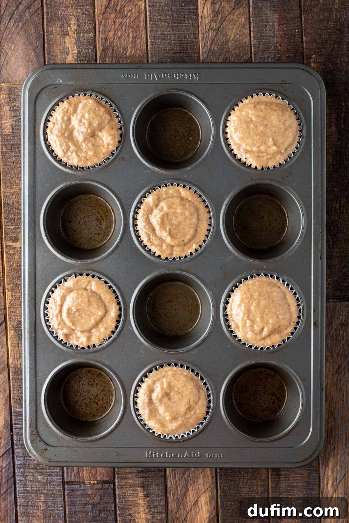 A metal muffin pan filled with thick applesauce muffin batter, ready for baking.