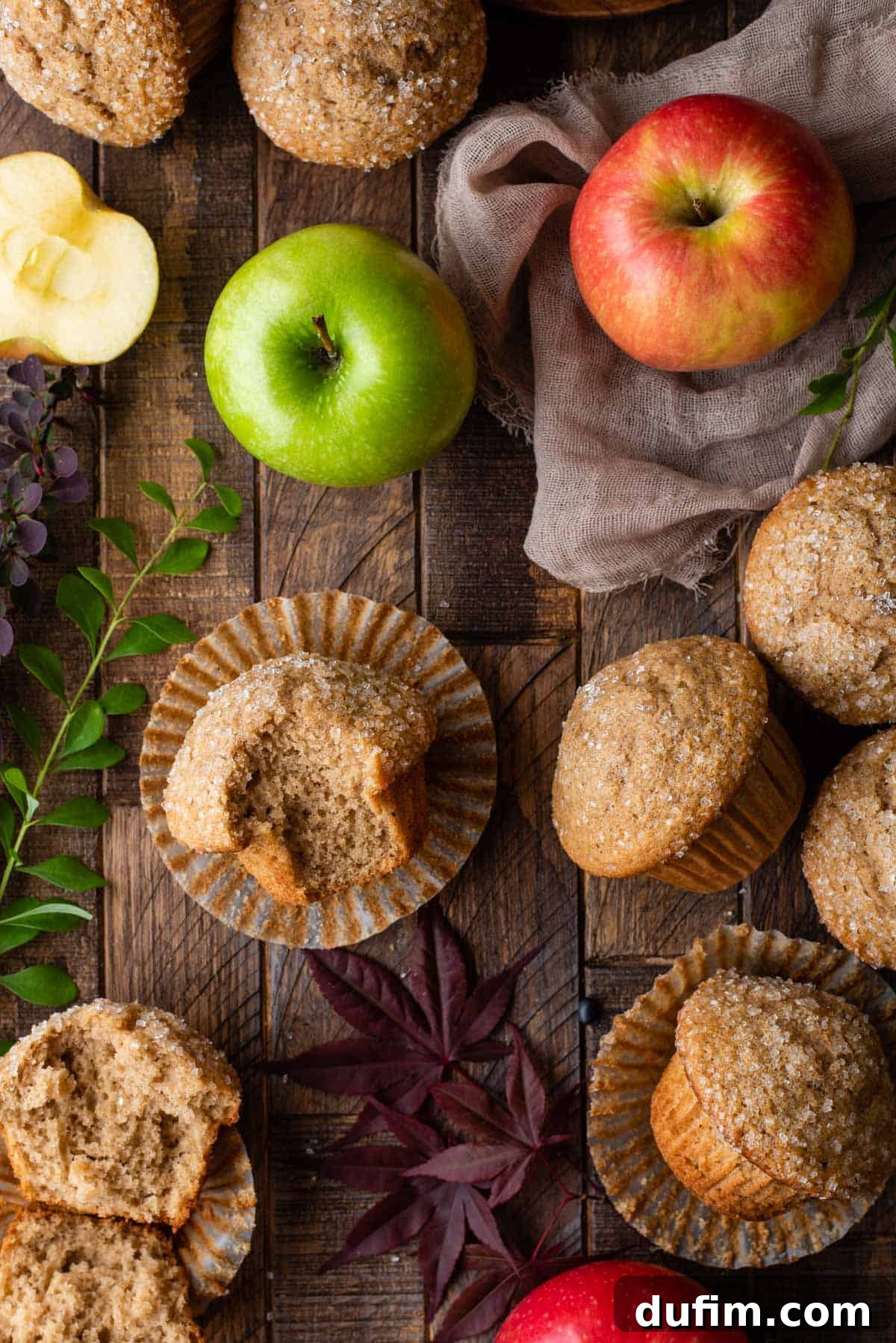 Applesauce muffins arranged on a rustic wooden background with fresh apples and vibrant fall foliage, creating a cozy fall atmosphere.