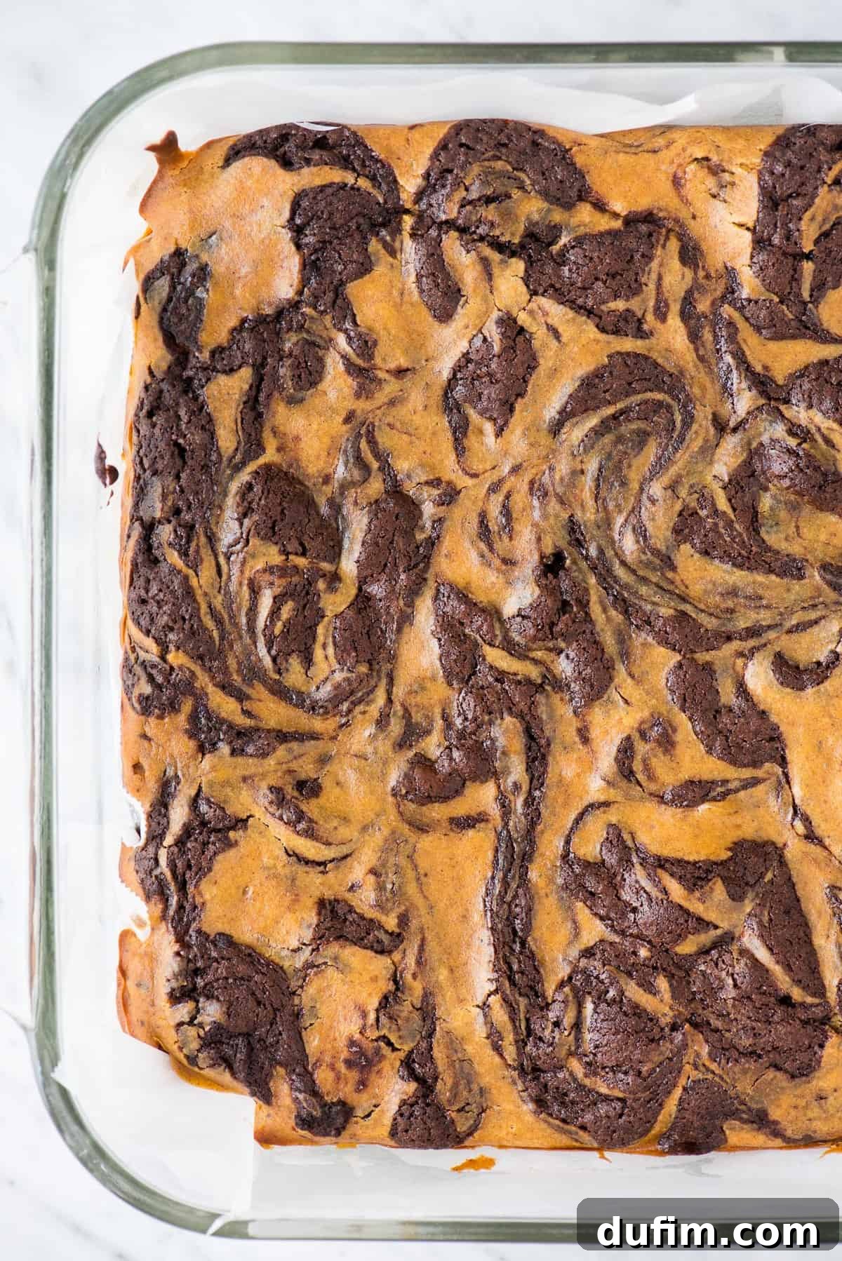 Pumpkin Cheesecake Swirl Brownies 5 Pumpkin swirled cheesecake brownies baking in a clear glass pan on a pristine white background, showcasing the beautiful marbling.