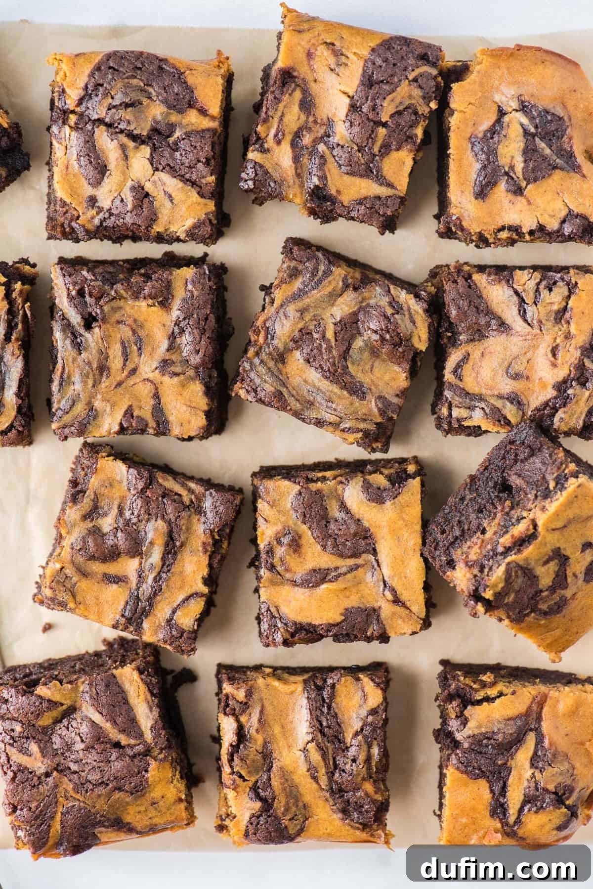 Pumpkin Cheesecake Swirl Brownies 7 Freshly baked pumpkin brownies, cut into 12 perfect squares and arranged on brown parchment paper, ready to be enjoyed.