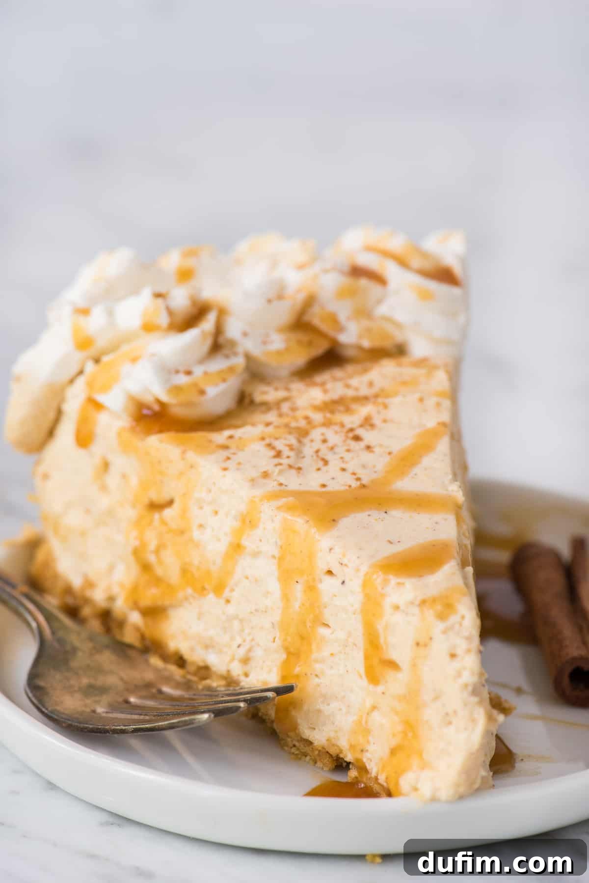Effortless Spiced Pumpkin Cheesecake 2 slice of no bake pumpkin cheesecake with caramel drizzle on top on white plate on white background