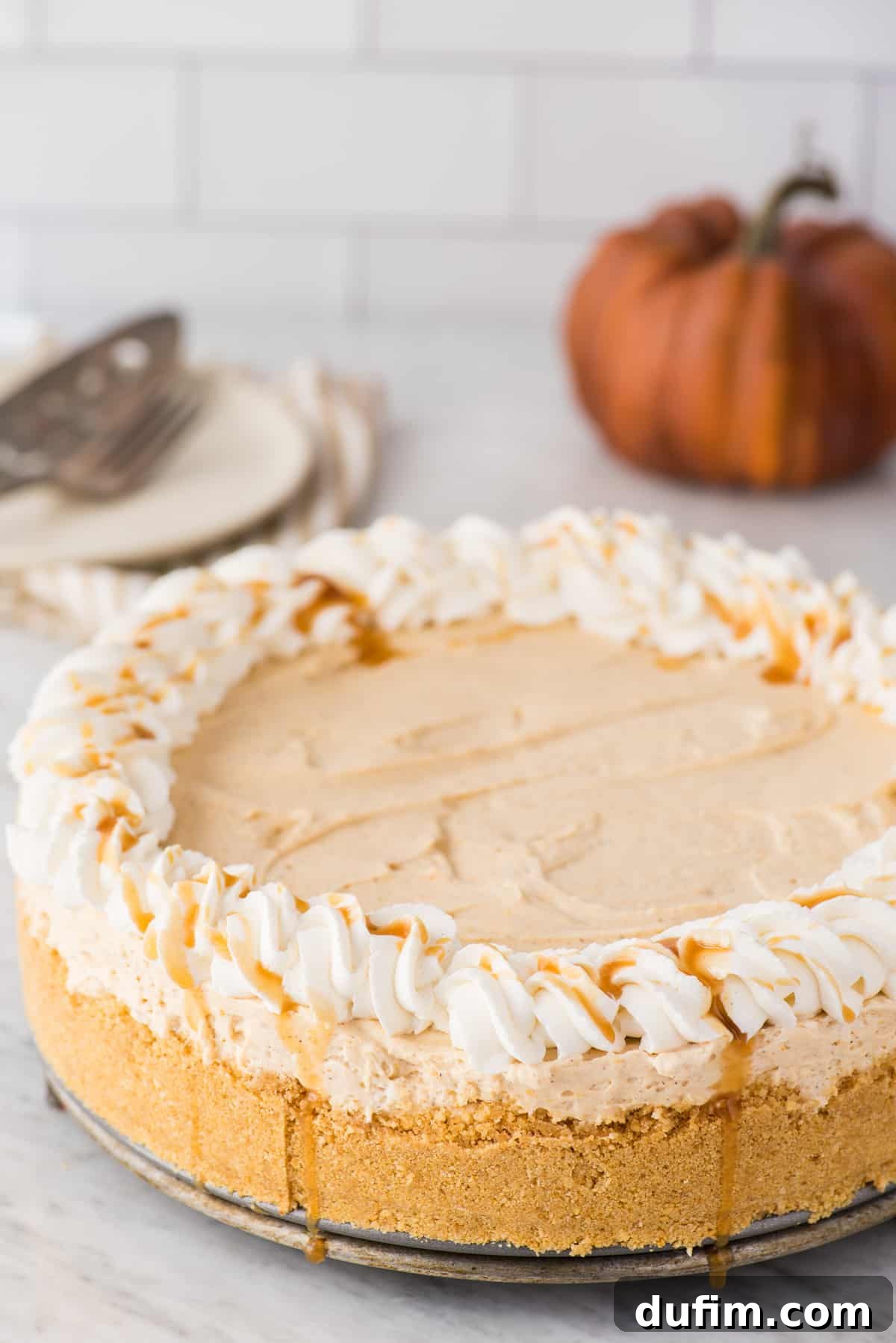 Effortless Spiced Pumpkin Cheesecake 3 a whole pumpkin cheesecake with whipped cream and caramel drizzle around the outside on white background