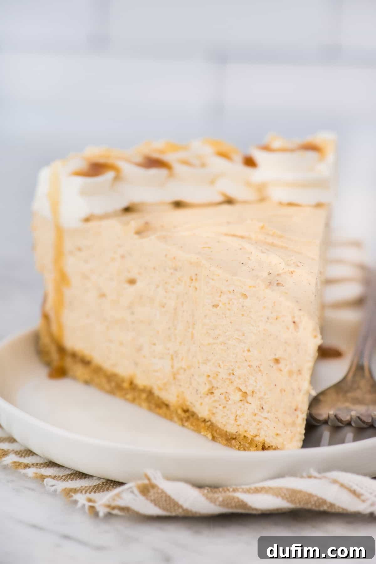 Effortless Spiced Pumpkin Cheesecake 7 a slice of no bake pumpkin cheesecake on white plate with striped linen underneath the plate with white background