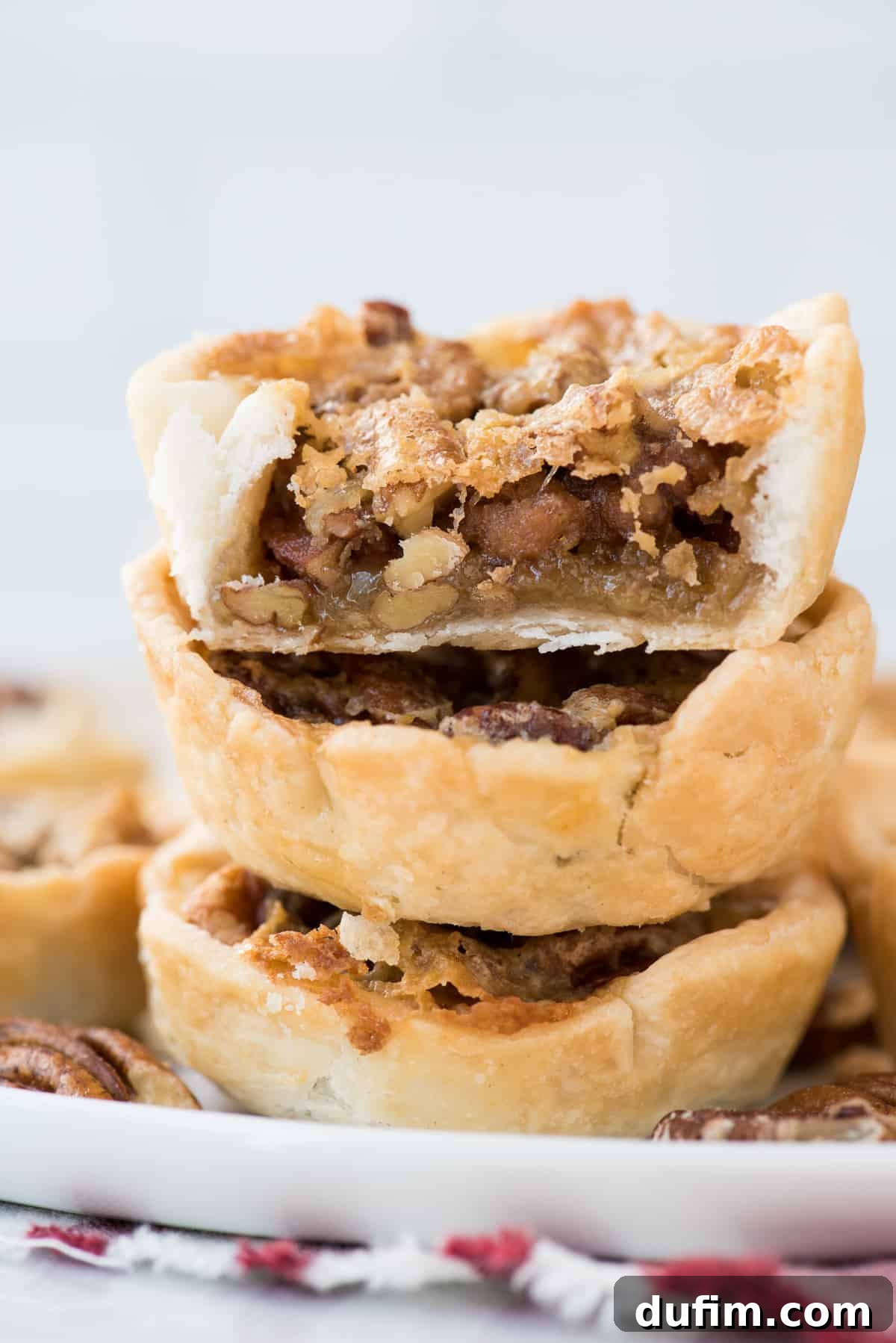 Three perfectly stacked mini pecan pies, with the top pie showing a delightful bite taken out, revealing the gooey, nutty filling and flaky crust, ready for enjoyment.