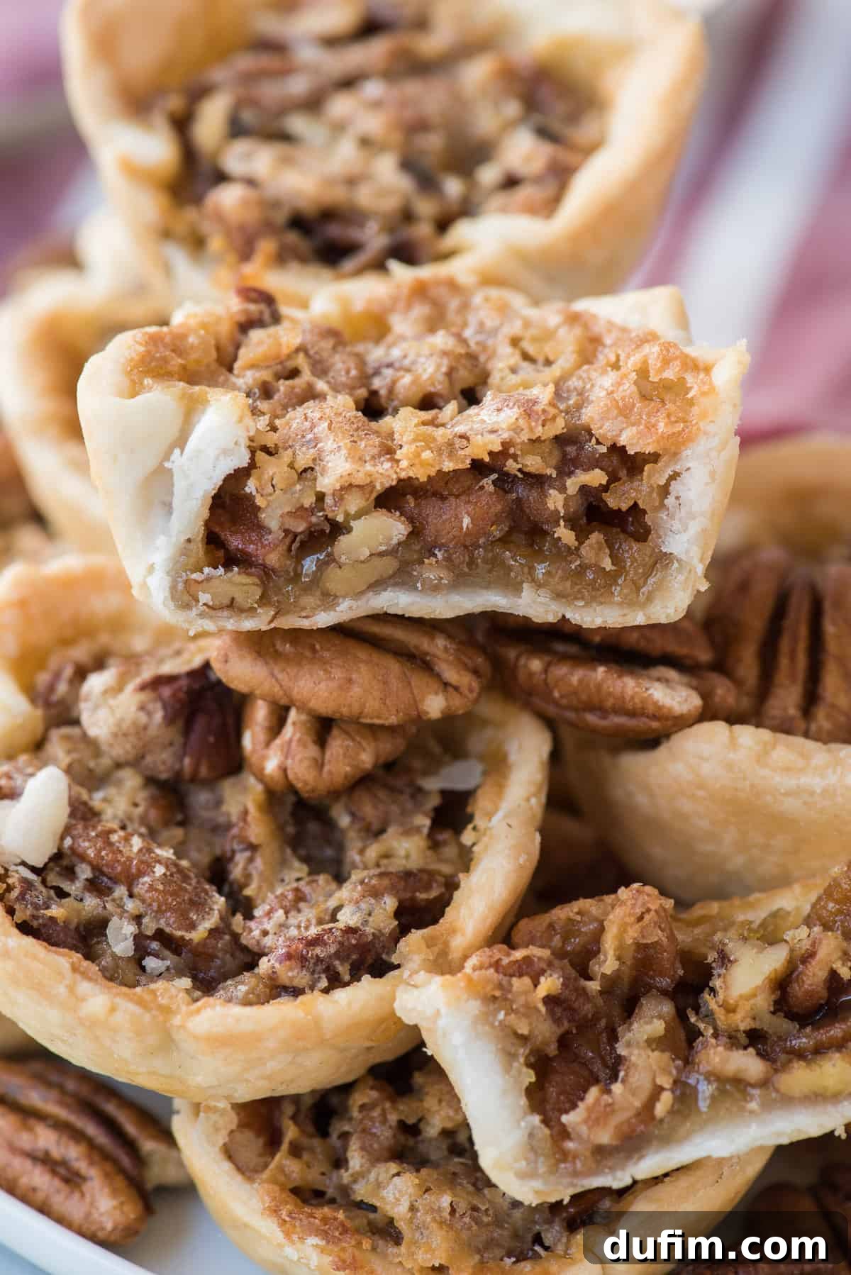 A charming pile of mini pecan pies, with the center pie having a bite removed, showcasing its delicious texture and inviting appearance.