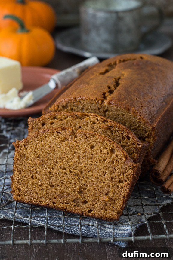 Starbucks Inspired Pumpkin Bread Perfection 3 A perfectly baked pumpkin bread loaf, sliced into two thick pieces, rests invitingly on a metal cooling rack. The moist interior and spiced aroma are palpable, ready to be enjoyed.