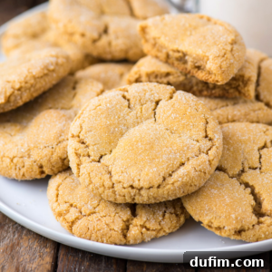Cozy Pumpkin Cookie Bliss 10 A plate of golden, pumpkin sugar cookies with cracked tops, stacked and overlapping on a wooden table. Some cookies are whole, while one is broken in half to reveal its soft interior.