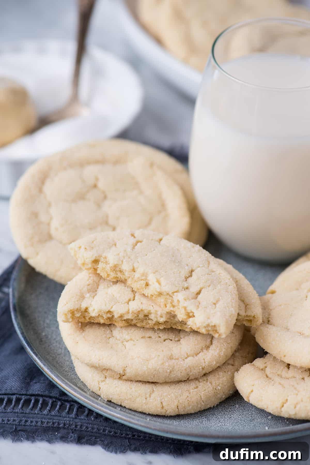Rolled sugar cookies arranged on a blue plate with a glass of milk in the background, creating a cozy and inviting scene.