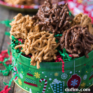 A festive green tin filled with clusters of chocolate and butterscotch haystack cookies, also known as haystack candy, nestled in red and green crinkled paper. The tin is decorated with cheerful holiday-themed patterns.