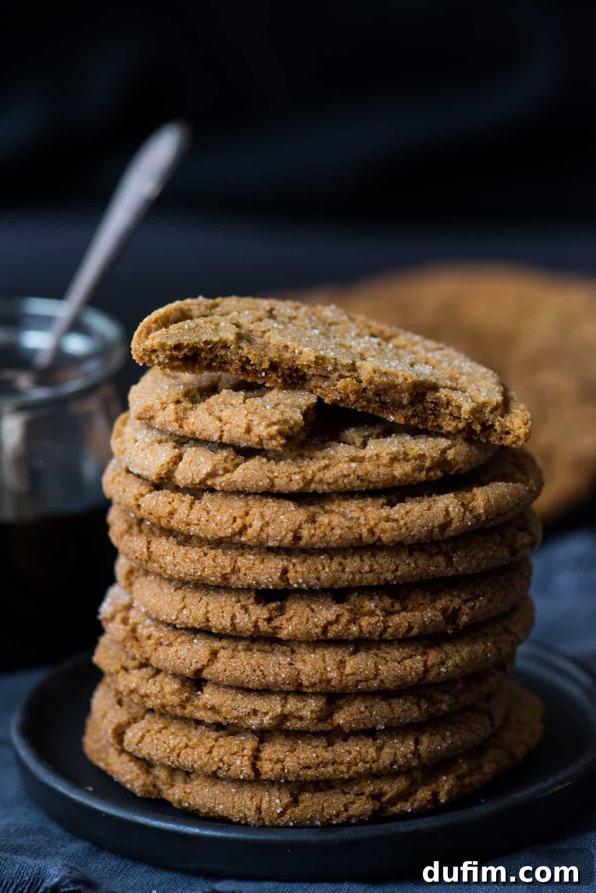 Ultimate Chewy Ginger Molasses Cookies 3 Stack of ginger molasses cookies on a dark plate, with more cookies and a bottle of molasses in the background, showcasing their rich color and inviting texture.