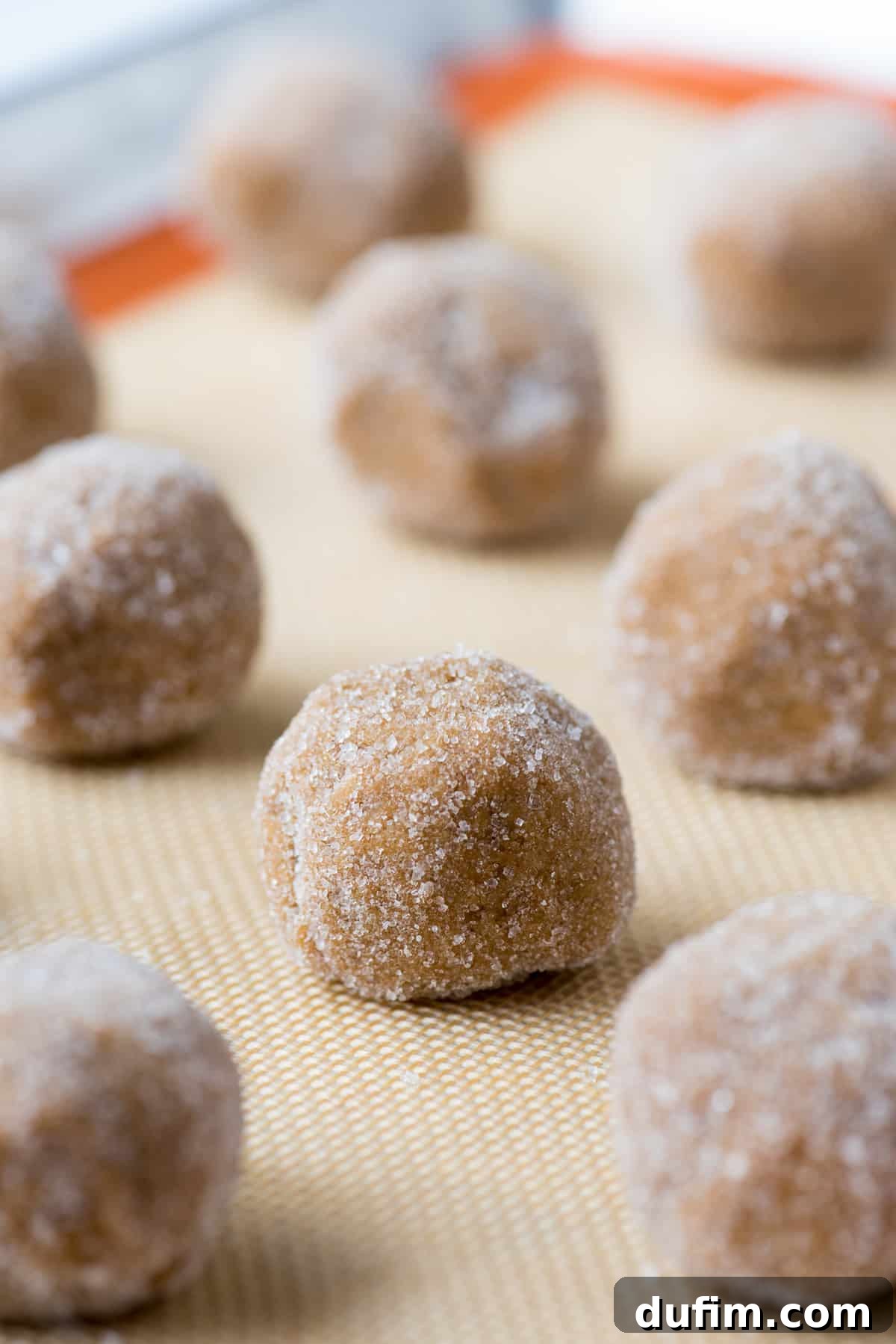 Ultimate Chewy Ginger Molasses Cookies 4 Ginger molasses cookie dough balls, coated in sugar, neatly arranged on a silicone baking mat before baking.