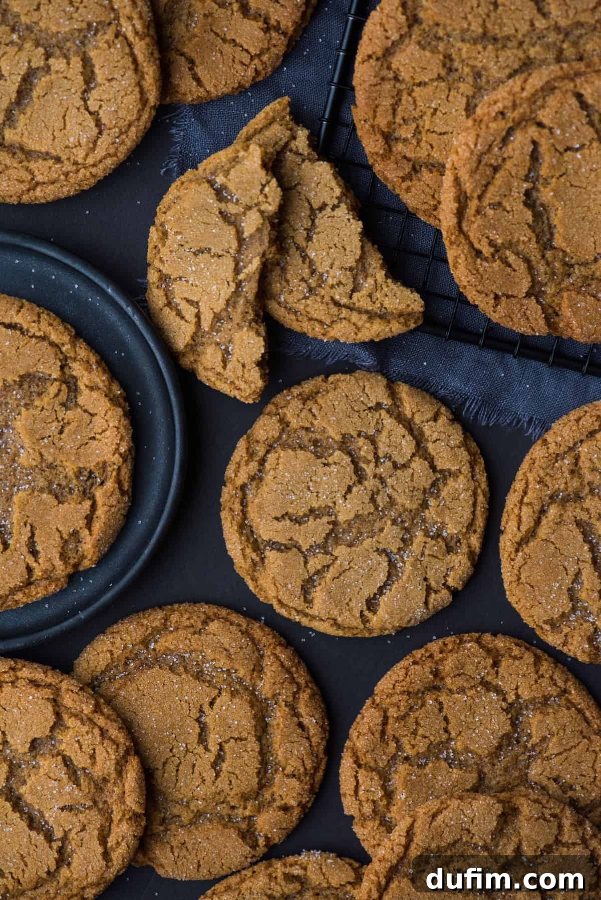 Ultimate Chewy Ginger Molasses Cookies 5 A collection of ginger molasses crinkle cookies artfully arranged on a dark background, with a dark plate and a black wire cooling rack, emphasizing their elegant presentation.