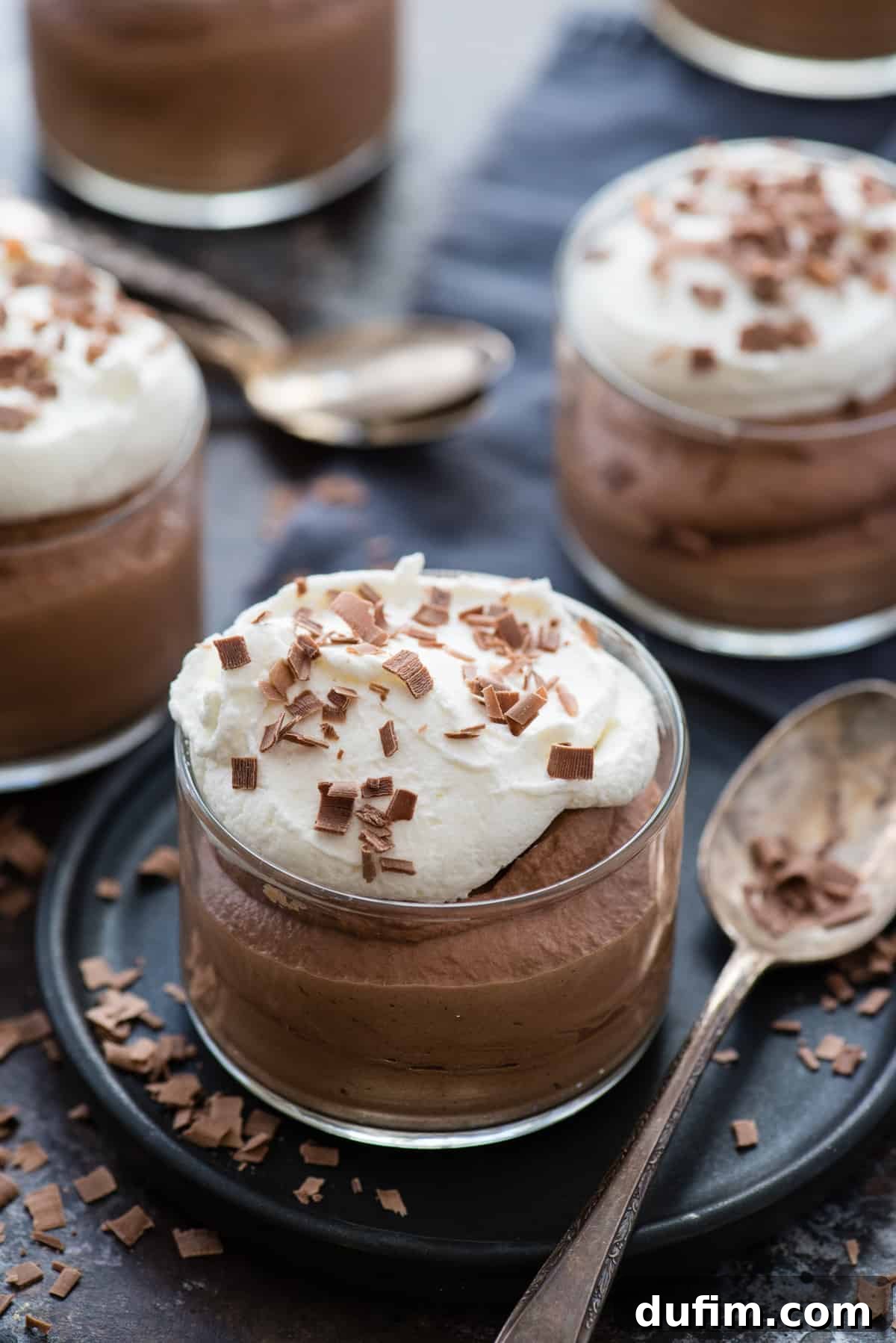 A glass bowl filled with rich, dark chocolate mousse, topped with a generous swirl of white whipped cream and delicate chocolate curls, ready to be served. The image captures the dessert's creamy texture and elegant presentation.